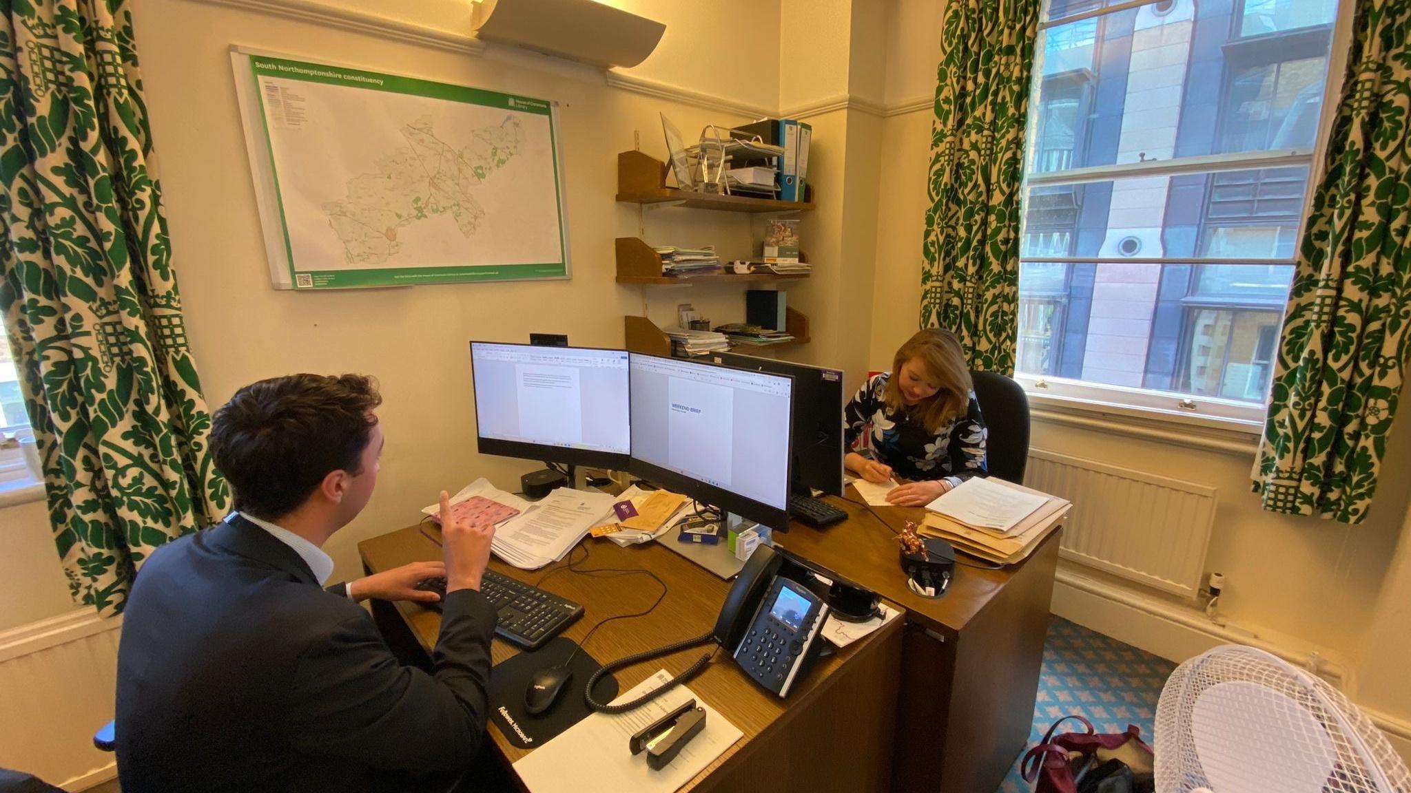 Sarah Bool in her office in Westminster with a map of her constituency on the wall and a colleague working opposite