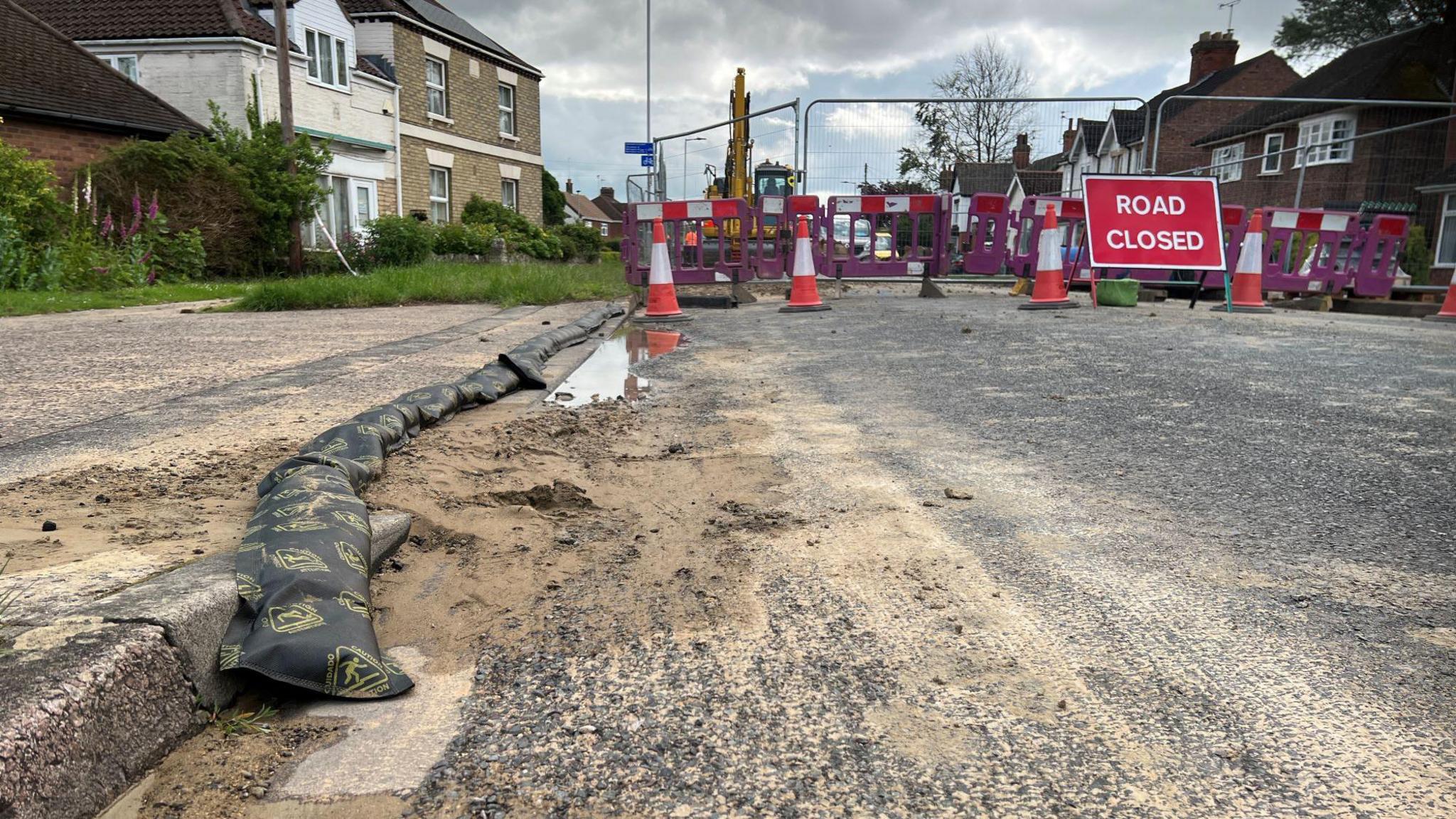 Sand on the road, with a road closed sign and fencing in the background