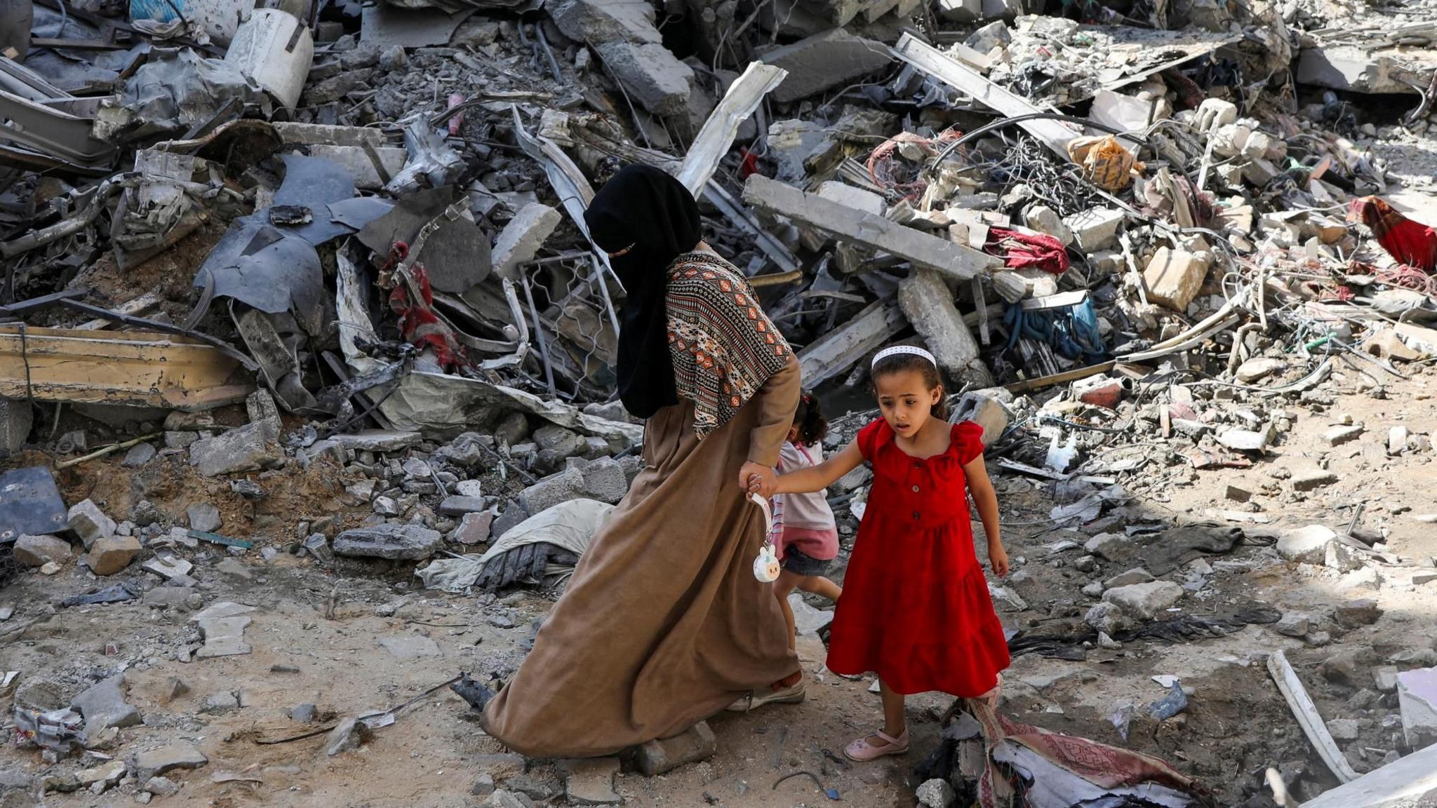 A Palestinian woman and a girl walk among debris after an operation by Israeli forces to rescue four Israeli hostages who were being held in Nuseirat refugee camp, in the central Gaza Strip (9 June 2024)