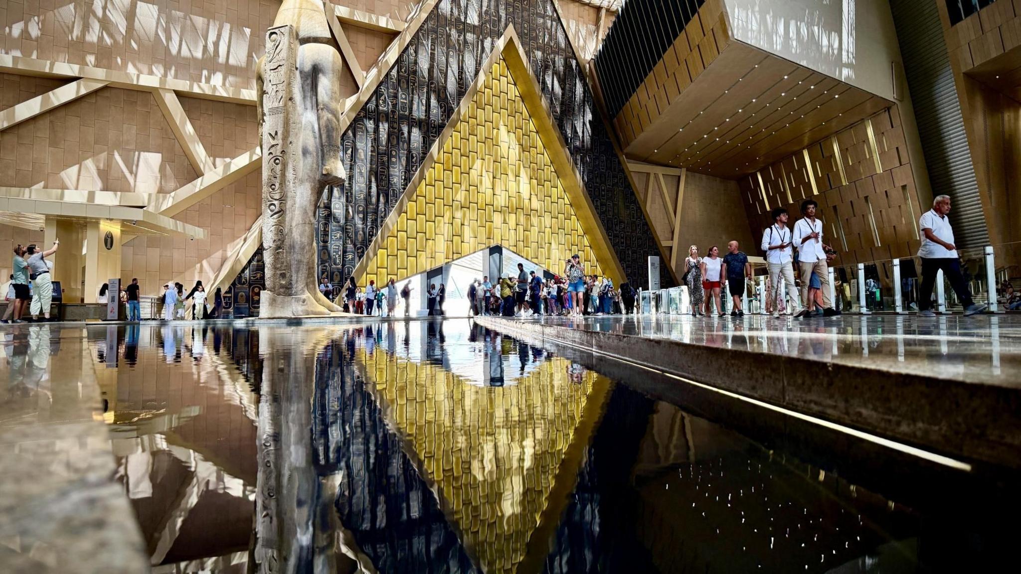 People walk next to a statue of King Ramses II in the main hall of the Grand Egyptian Museum, one of the country's most iconic monuments