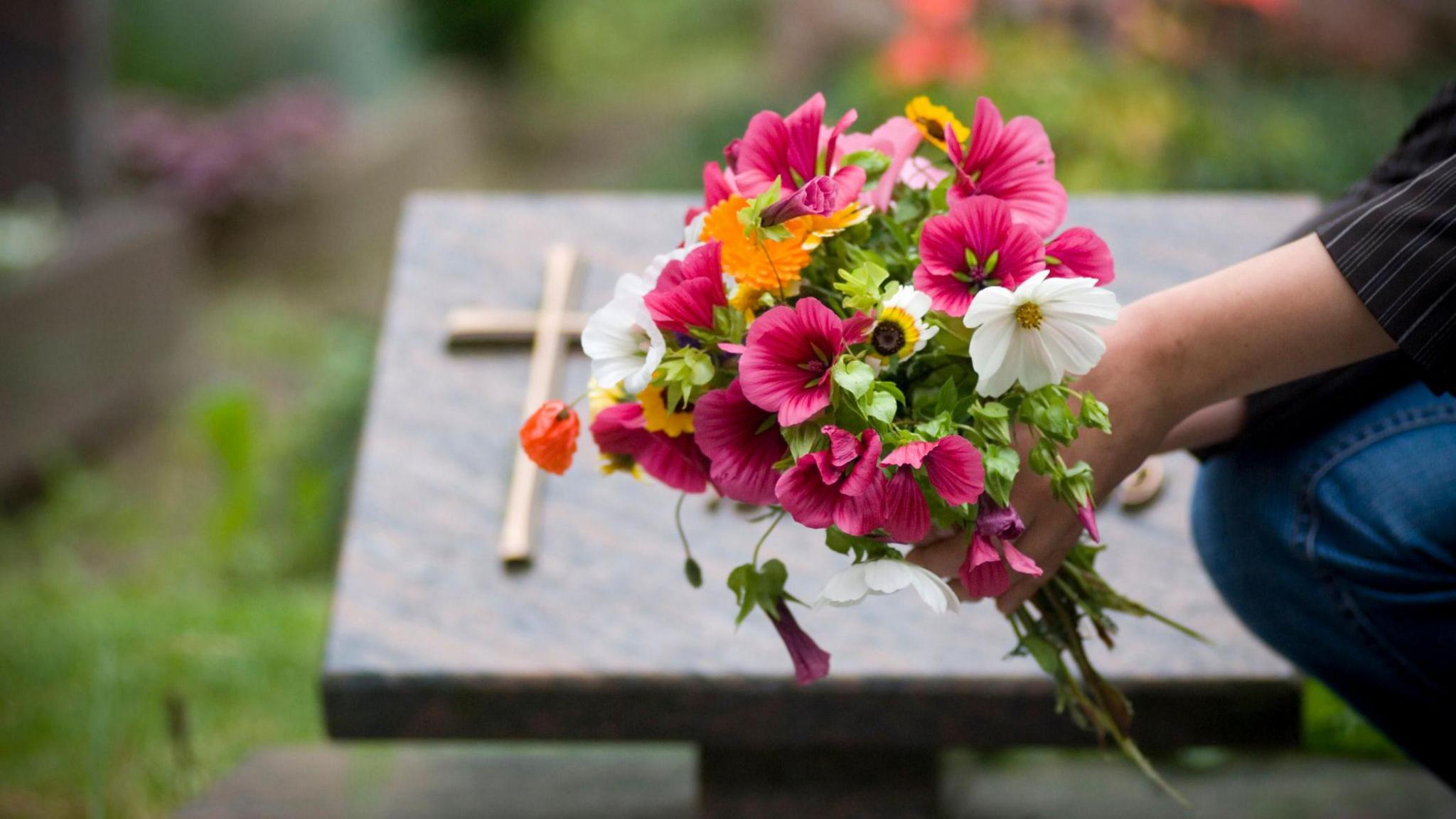 A person pictured laying flowers at a grave 