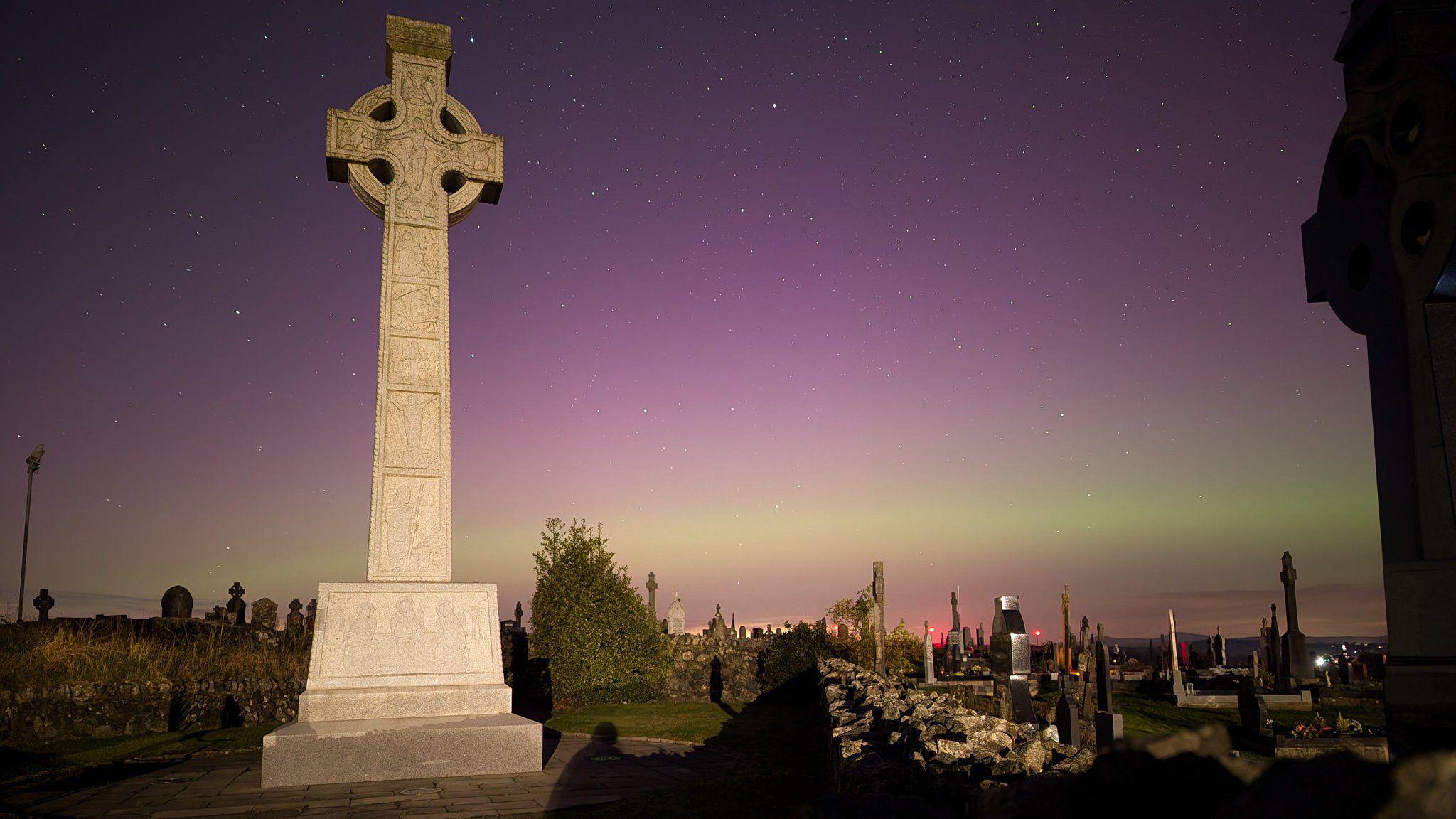 A grave stone with the northern lights in the background 