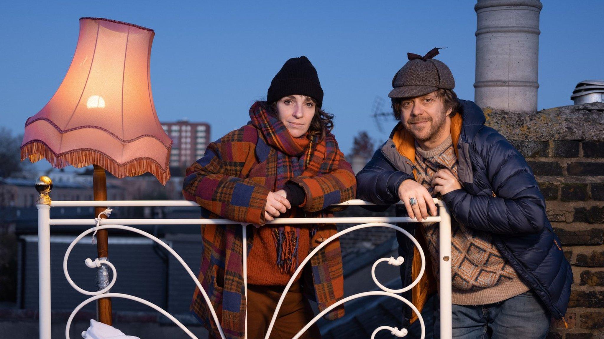 Dan and Hilary stand next to the bed on their roof