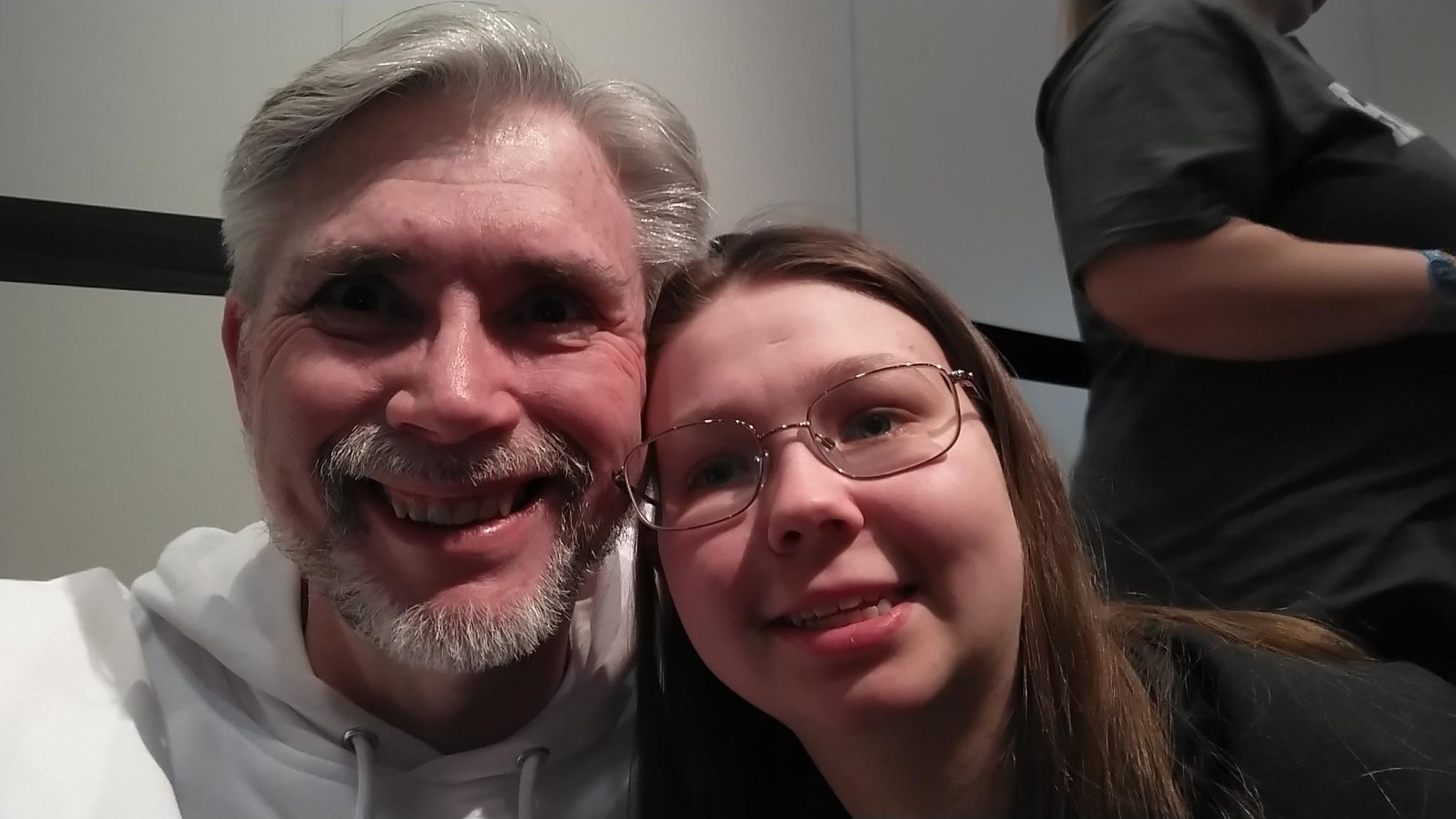 Richard and daughter Hollie. Both are looking to the camera and smiling. Hollie is wearing glasses and has long brown hair and Richard is wearing a white tracksuit top. 