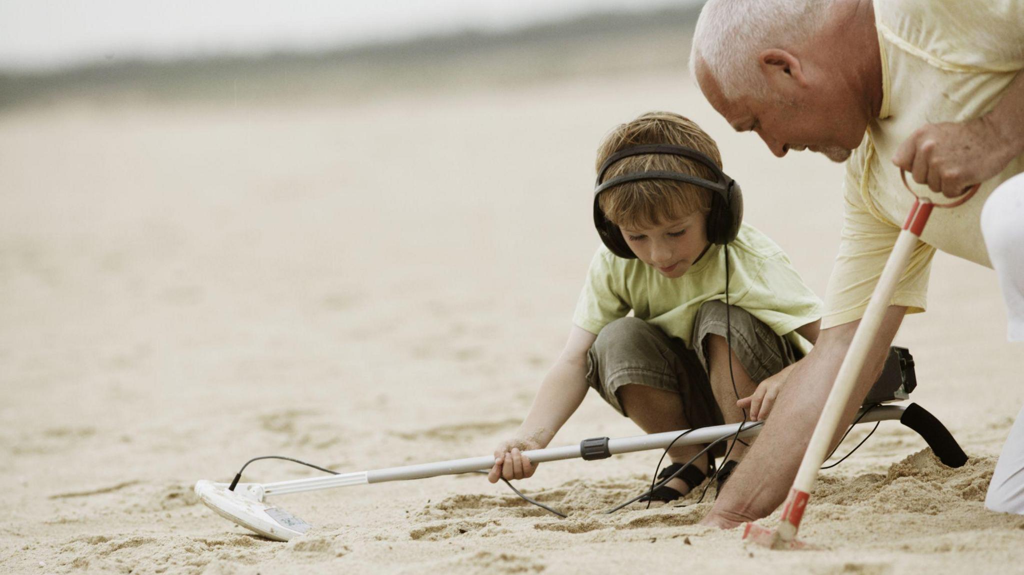 child and grandparent on beach with metal detector