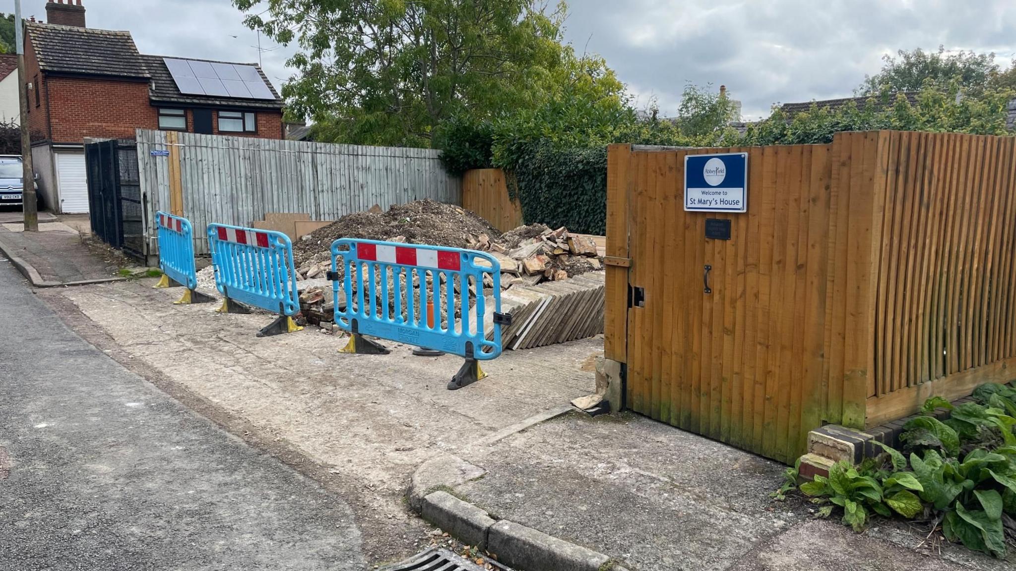 Material from patio work stored at the back entrance to St Mary's House which is a wooden fence attached to a wooden fence.