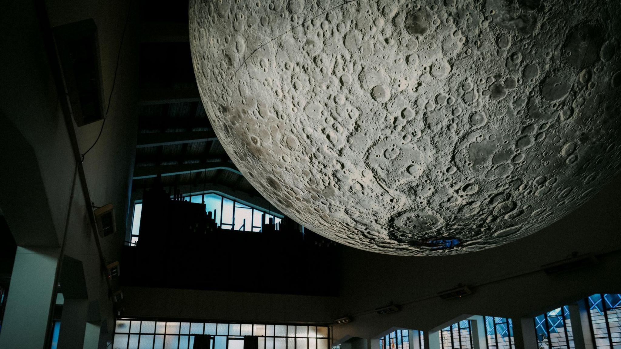 The art installation depicting the moon, put up in a church. It is very big art installation surrounded by stain glass windows. The room is dimly light.