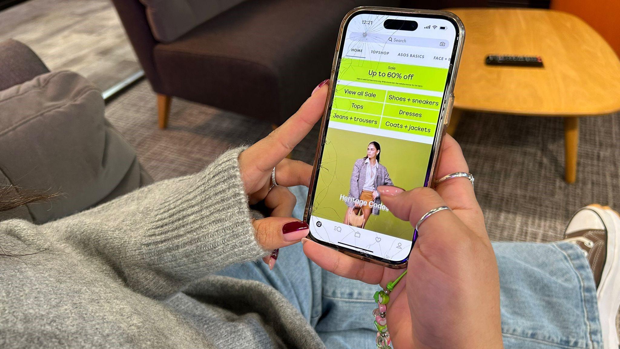 A view of a woman over her shoulder holding a phone with the ASOS app open