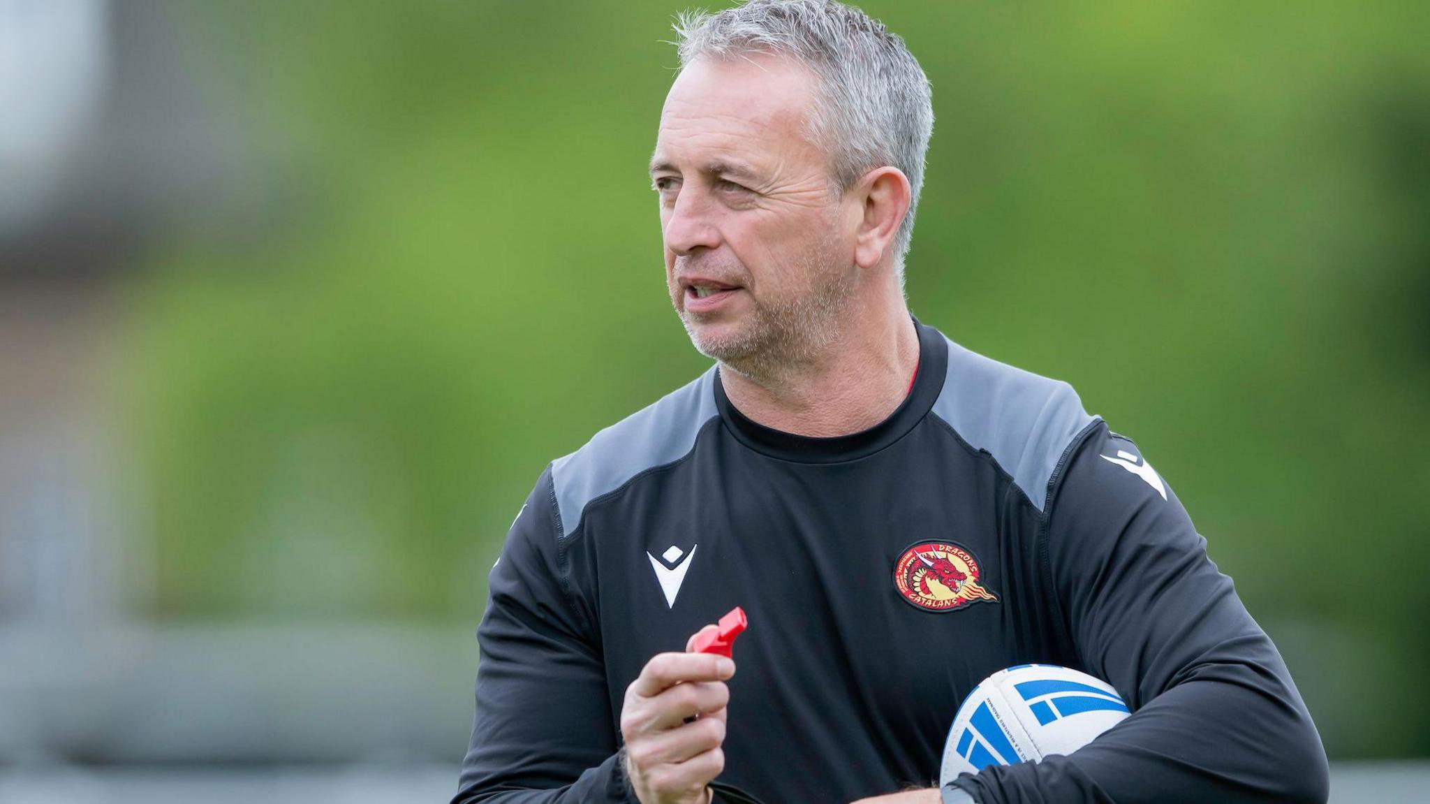 Former Catalans Dragons head coach Steve McNamara holding a rugby league ball and a whistle