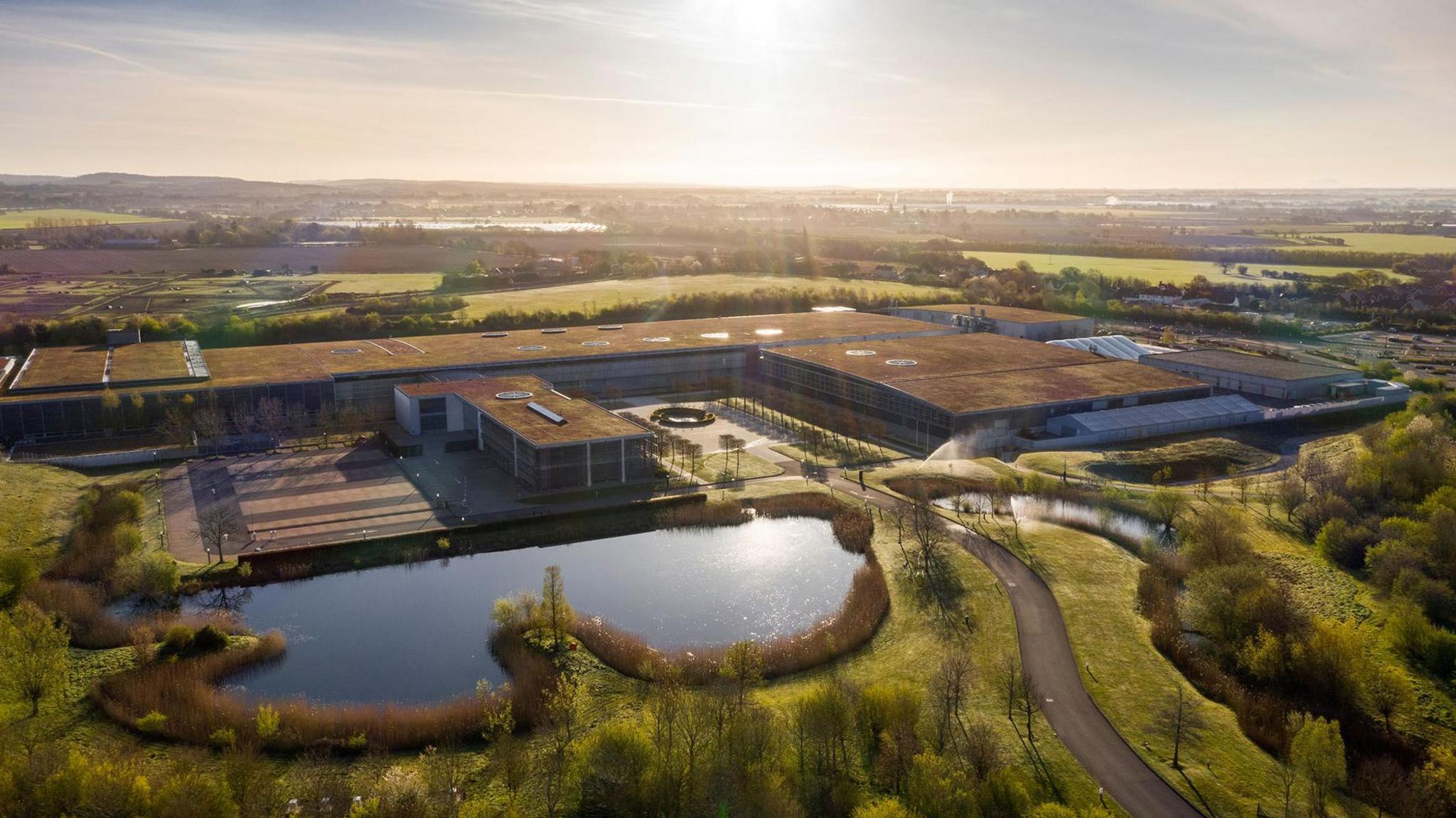 An aerial view of Rolls-Royce's Goodwood site in West Sussex with a sunburst and reflection on its lake