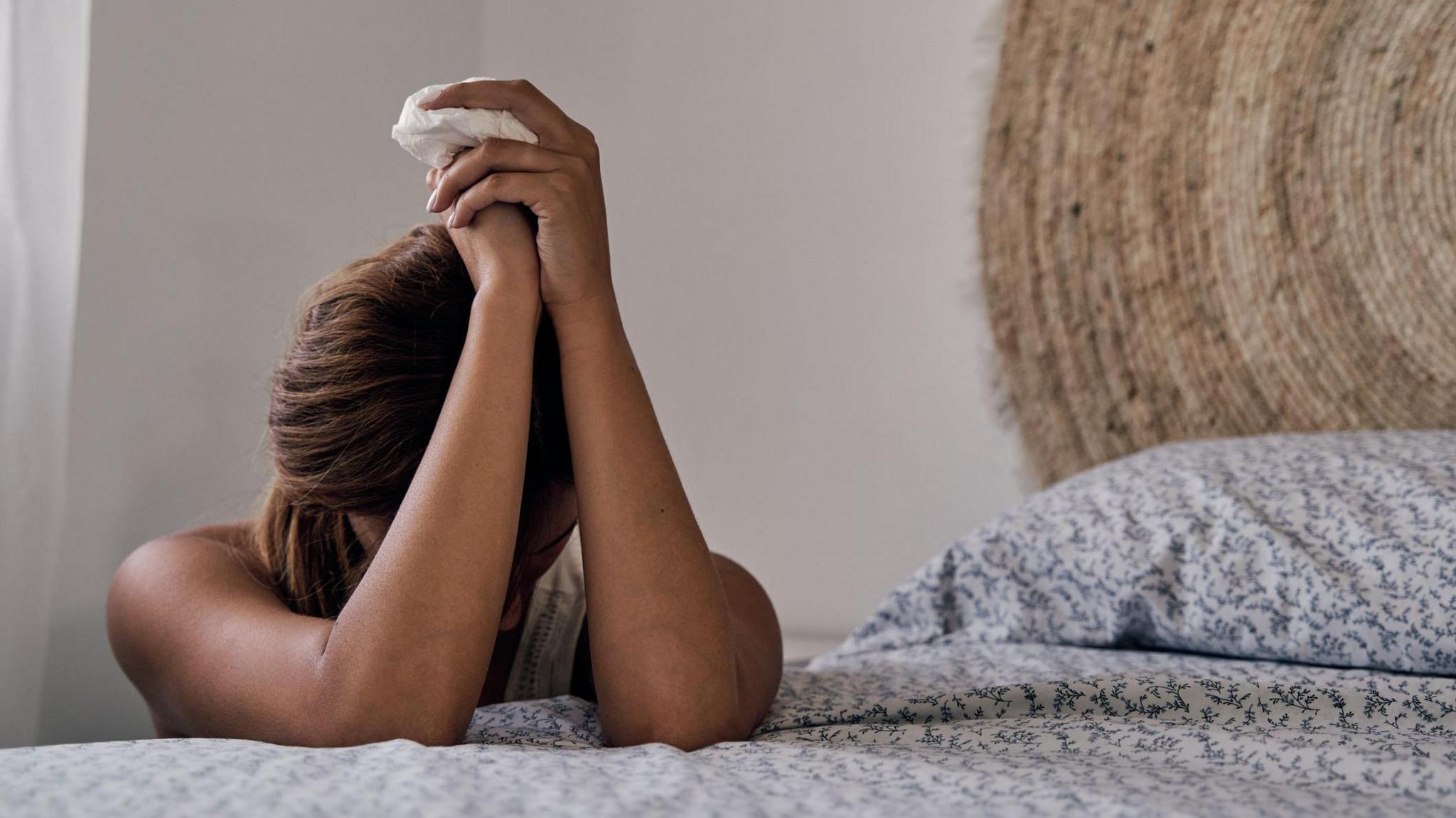 Unrecognizable abused woman lying on her bed with a tissue to dry her tears.