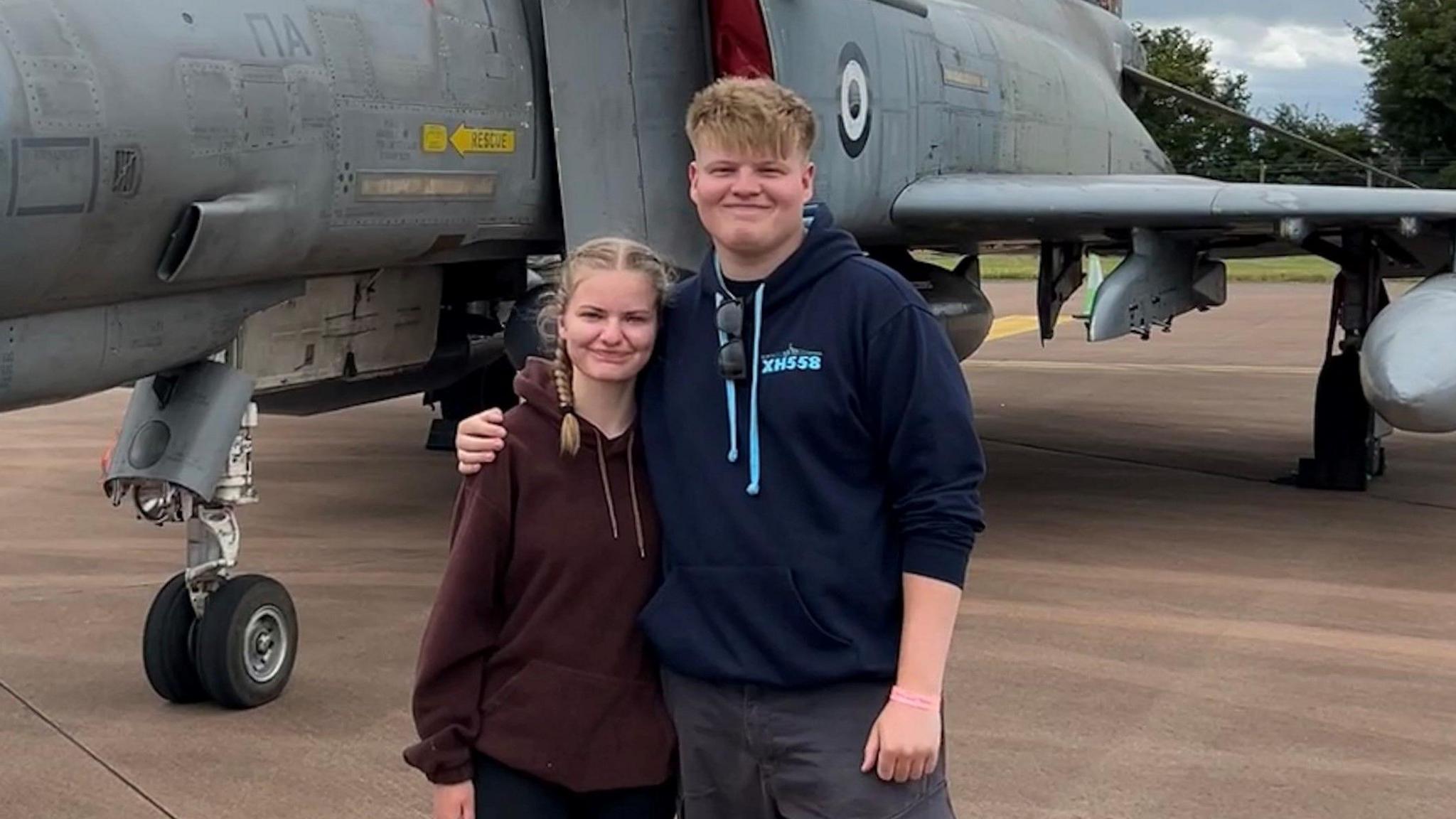 Emily Turner and Ben Smith in hoodies stood in front of a fighter jet