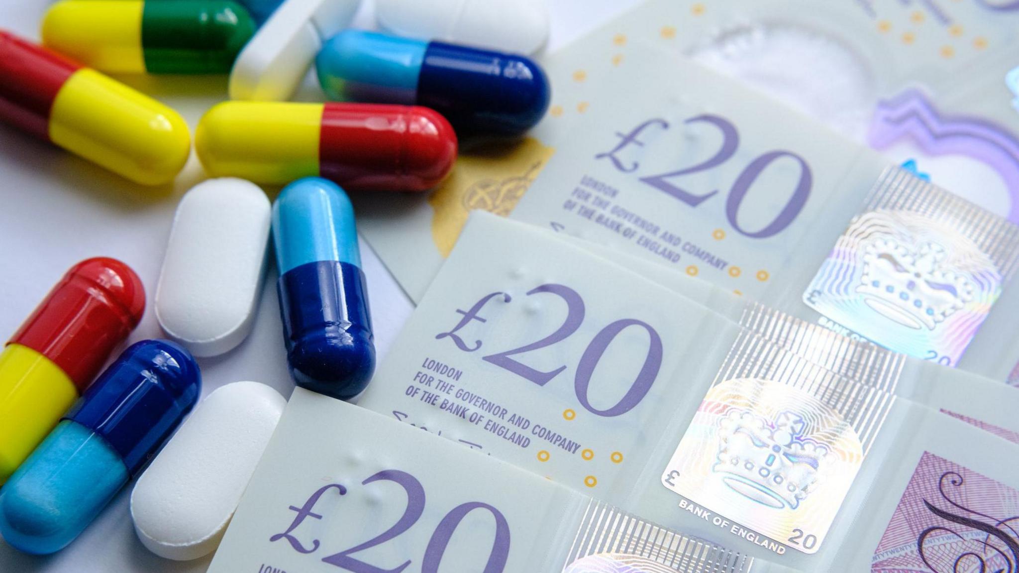 A pile of different colourful pills placed next to 20 British pound banknotes. - stock photo