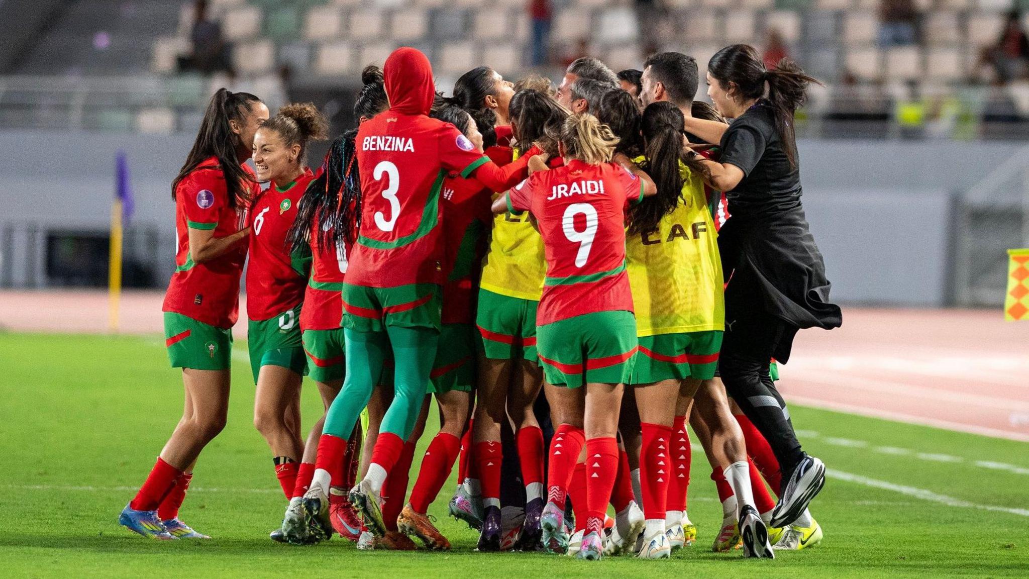 Morocco players and staff celebrate in a huddle on the pitch near the touchline after scoring a late equaliser against Zambia at the 2024 Women's Africa Cup of Nations