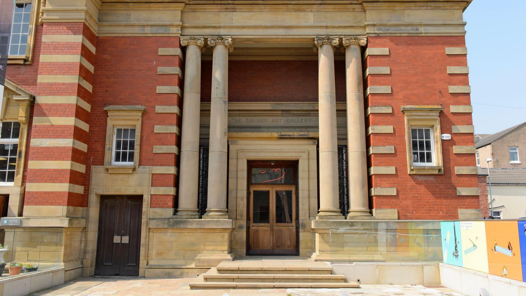 The Grundy Art Gallery is a mix of red and beige brick, it has two columns either side of the door