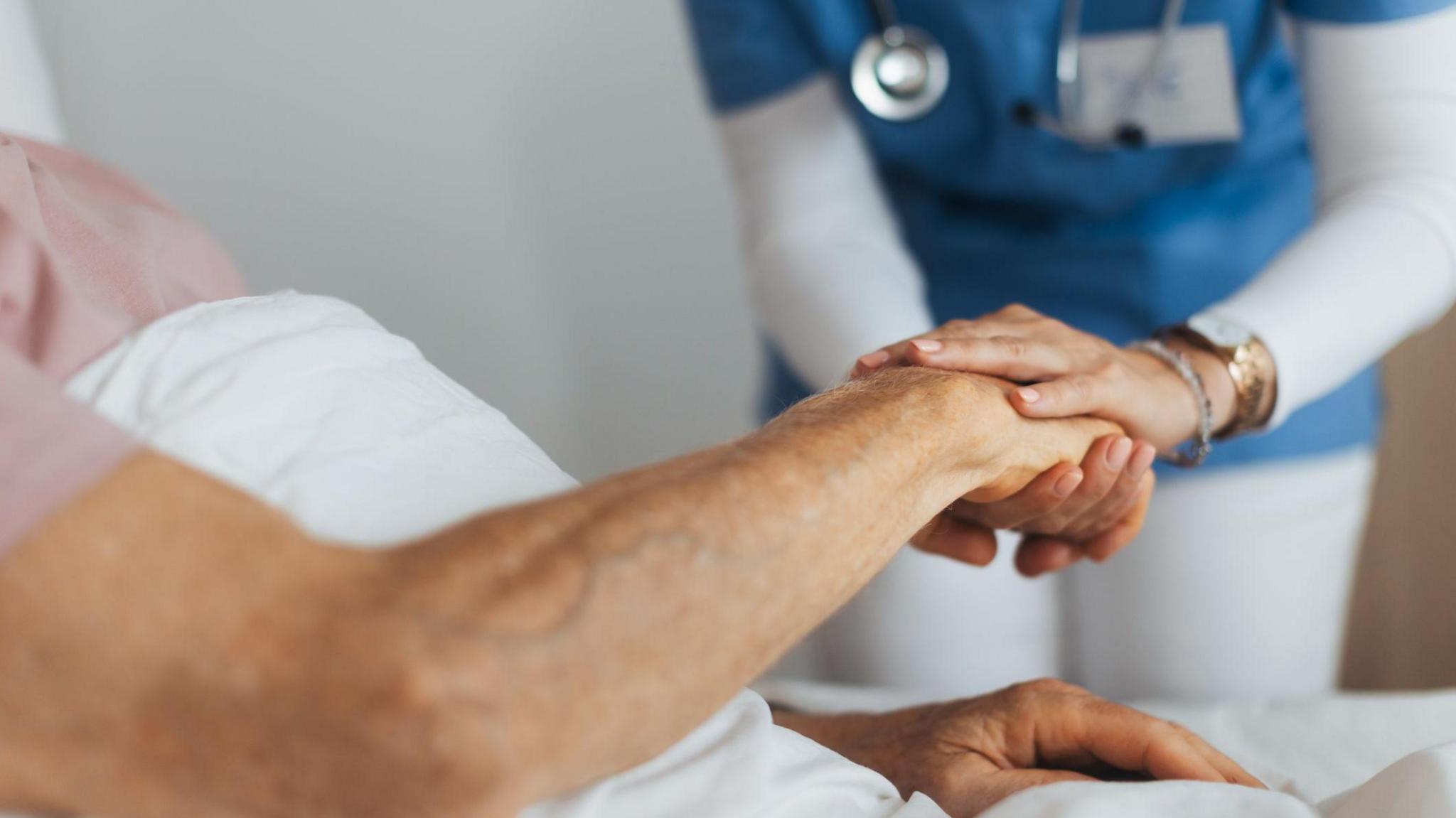 Stock image of a hospital patient in bed, holding a doctor's hand.