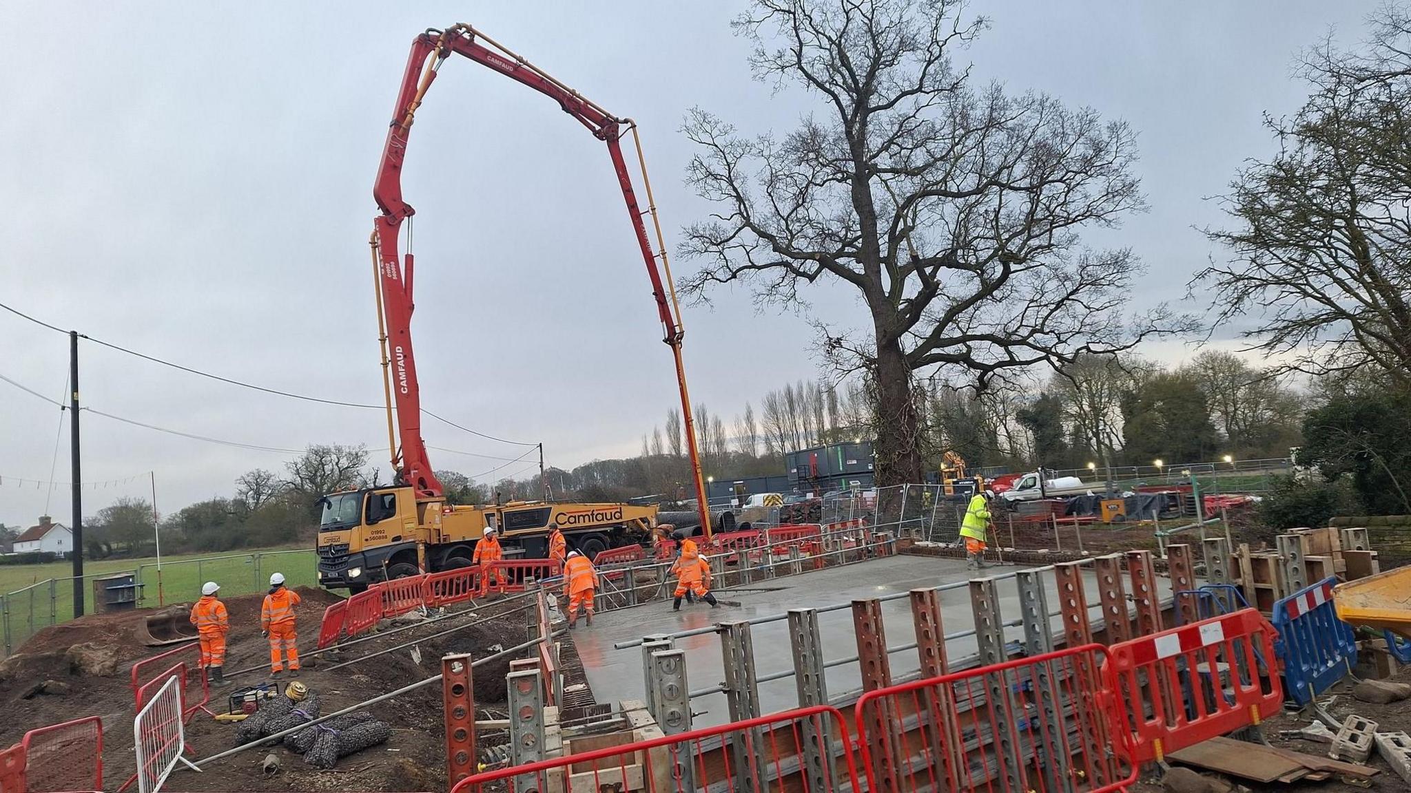 Highways workers and machinery can be seen on a building site for the construction of the new bridge. The area has been cordoned off and mud surrounds the site.