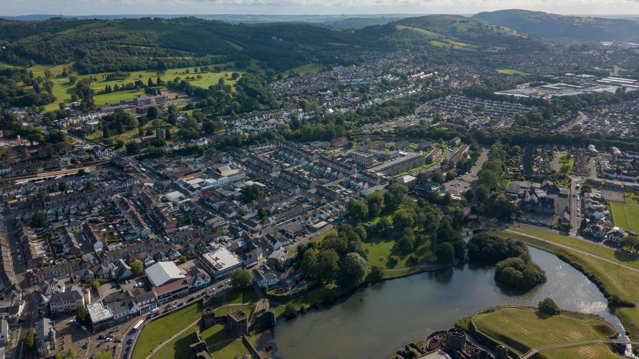 A drone shot of Caerphilly town with a lake seen in the foreground of the image with residential streets and housing behind it.