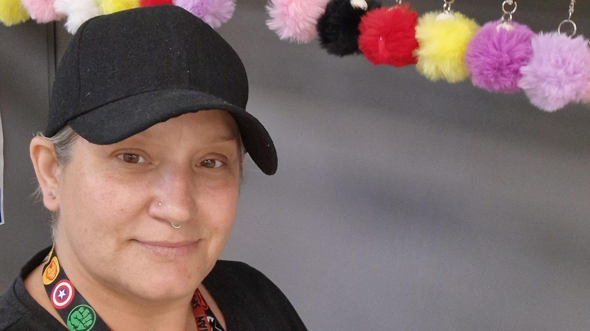 Charlotte Leak is smiling at the camera. She is wearing a black cap and has a gold nose piercing.