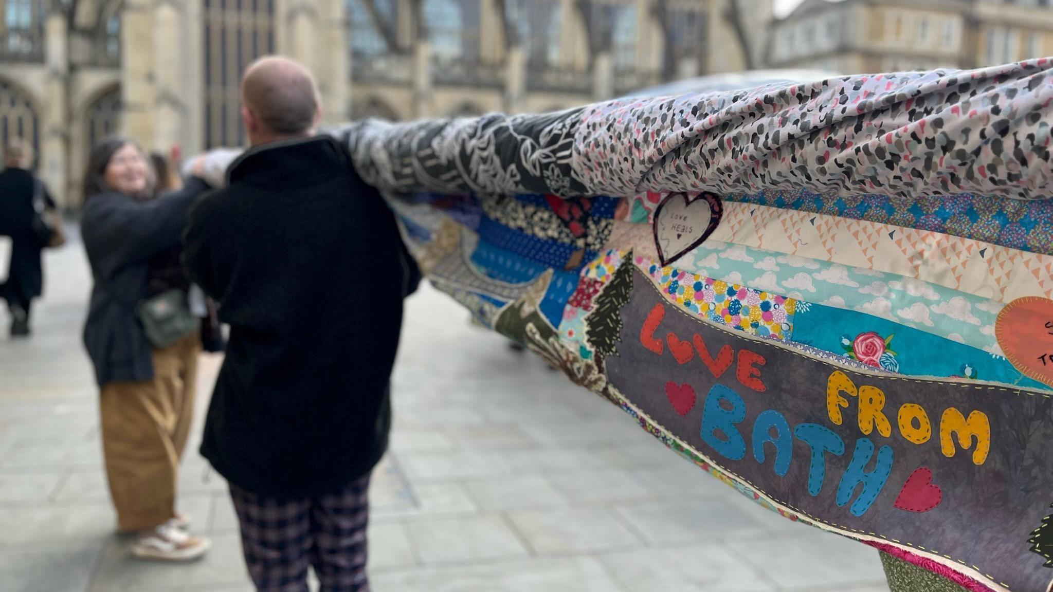 A group carrying a banner to Bath Abbey in the distance, with a square saying "love from Bath".