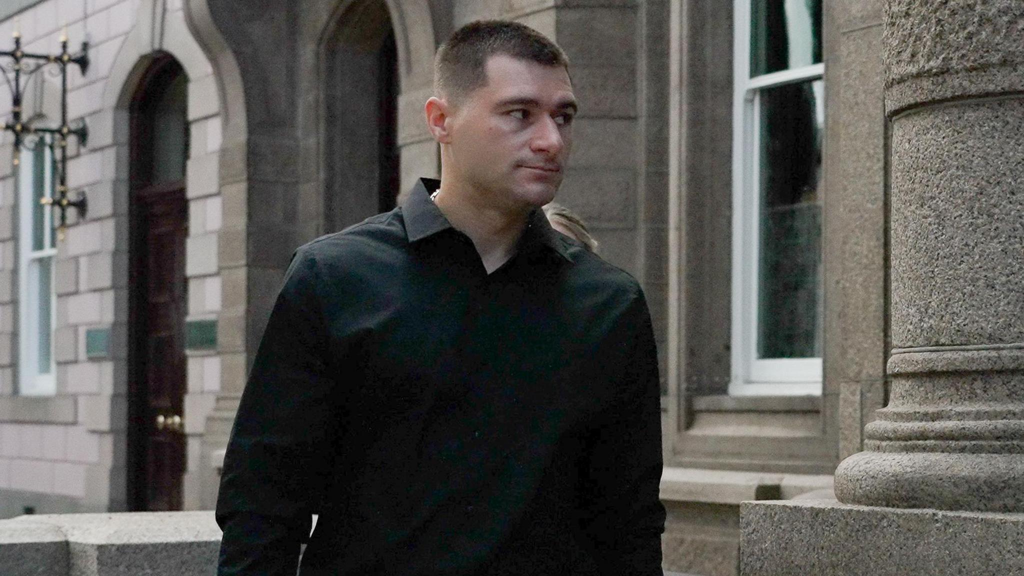 Artur Sevash-Zade walks into Jersey Royal Court. He is wearing a black shirt. He has short black hair.