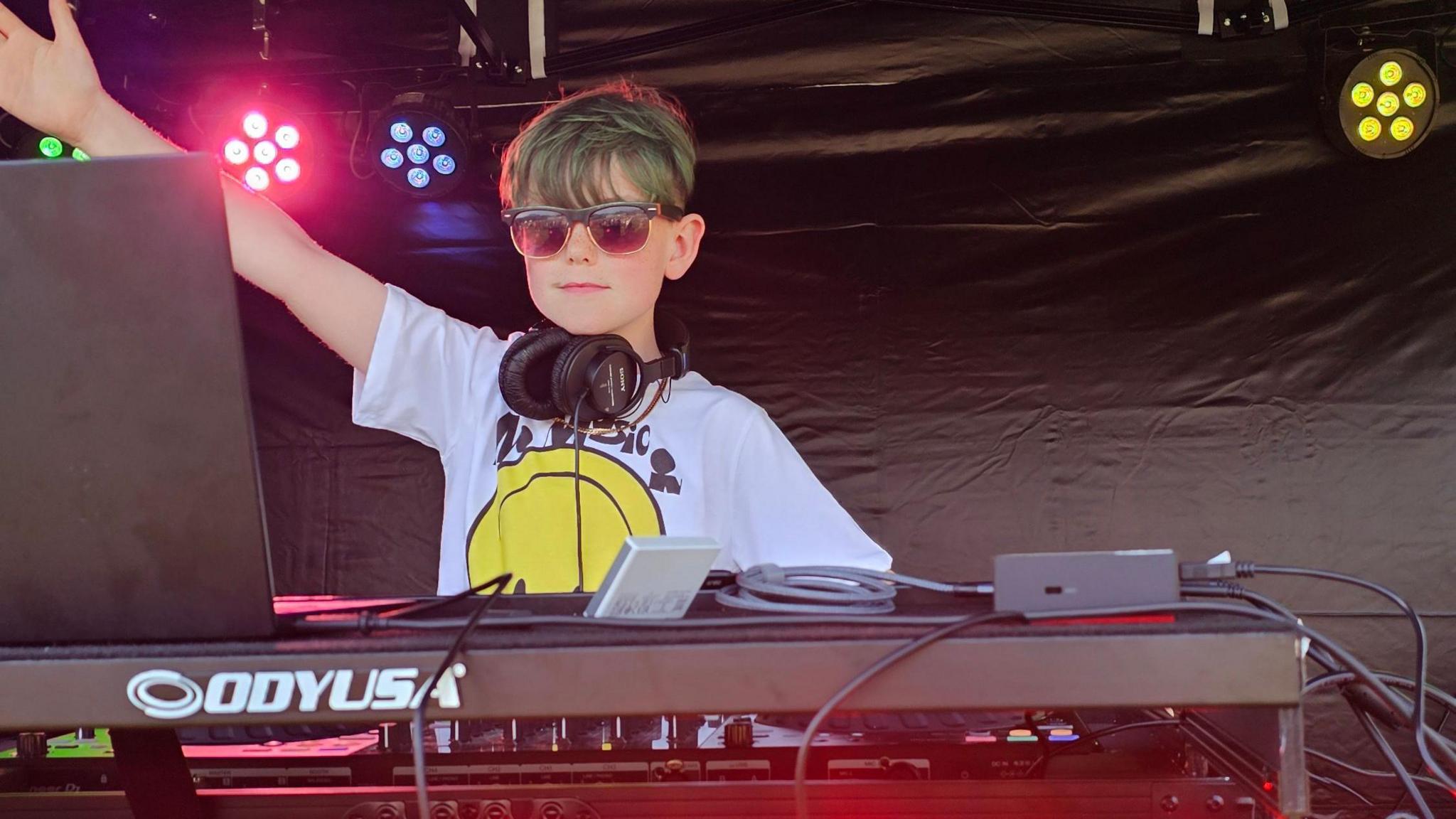 Efan Electro on stage with a pair of headphones around his neck and wearing sunglasses