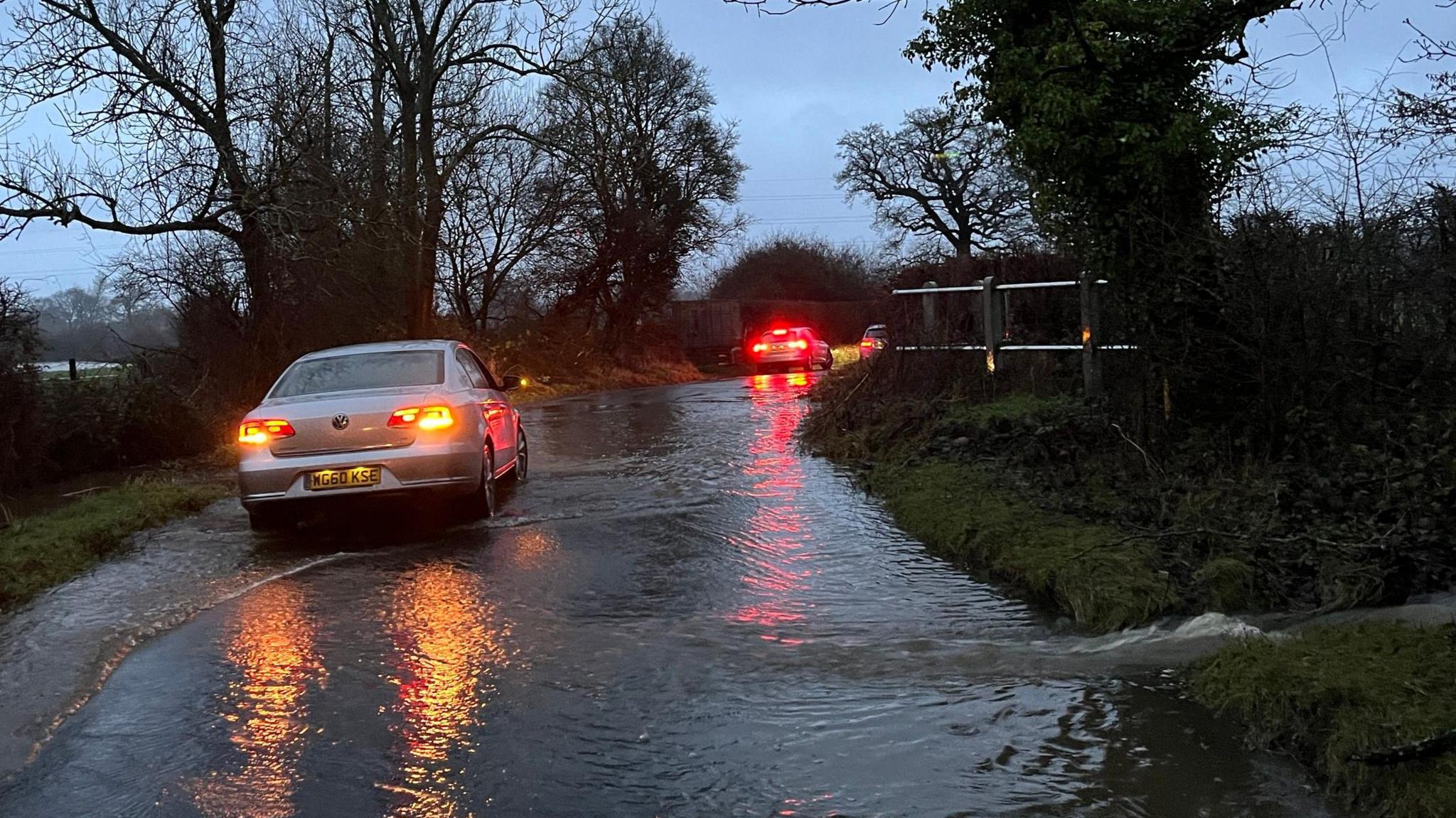 Two cars passing heavy flooding in a county  lane