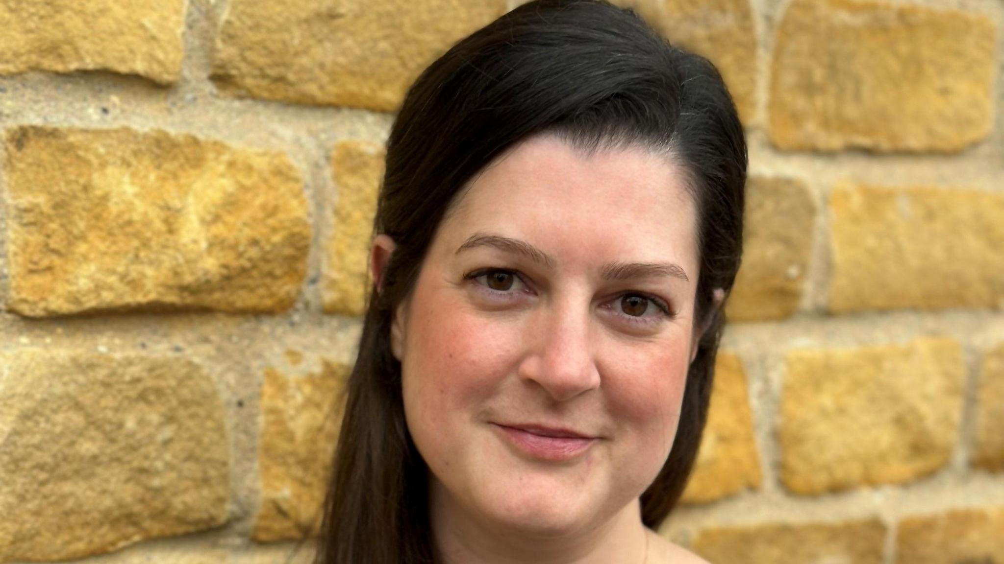 Profile picture of woman with long black hair standing in front of a brick wall