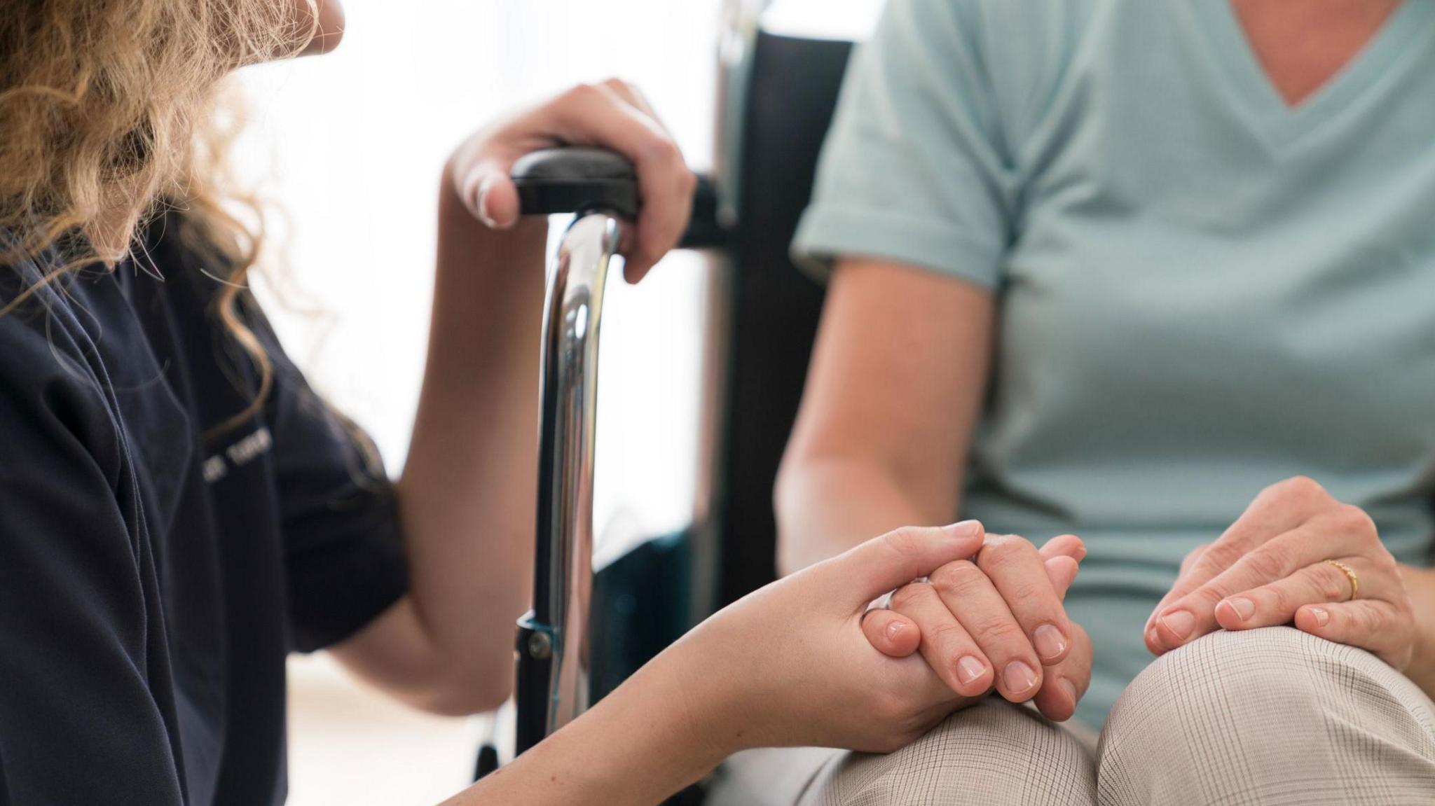 Stock image of a carer holding the hand of someone in a wheelchair