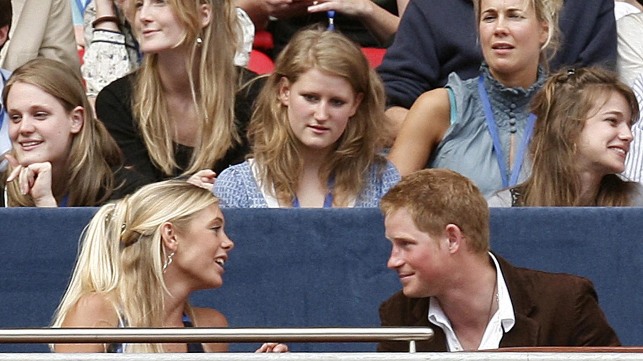 Chelsy Davy and Prince Harry are looking directly at each other. They are seated next to each other at an event and other people can be seen in the rows behind them