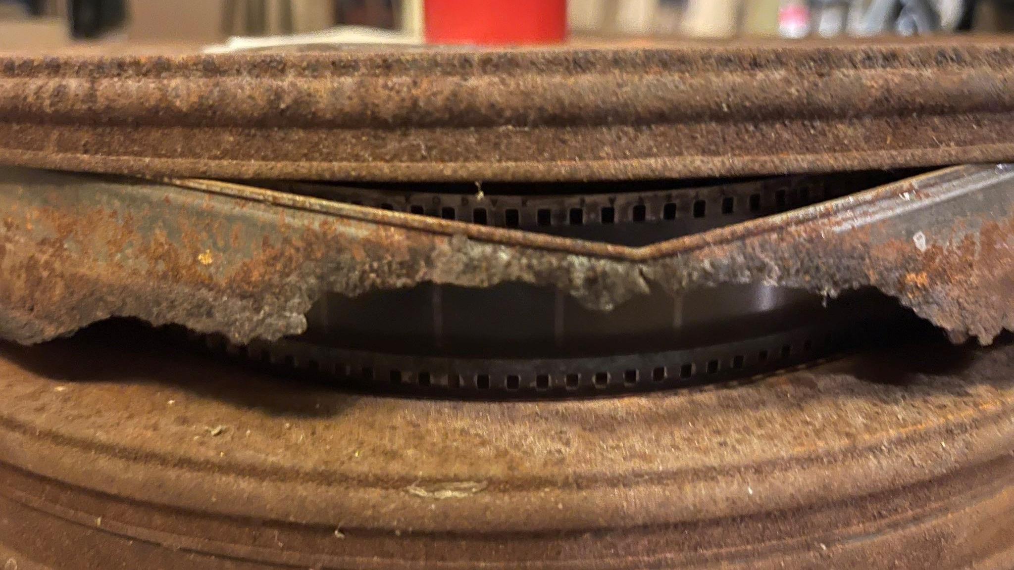 A metal container that has appeared to split open at the side, exposing the film reels inside.