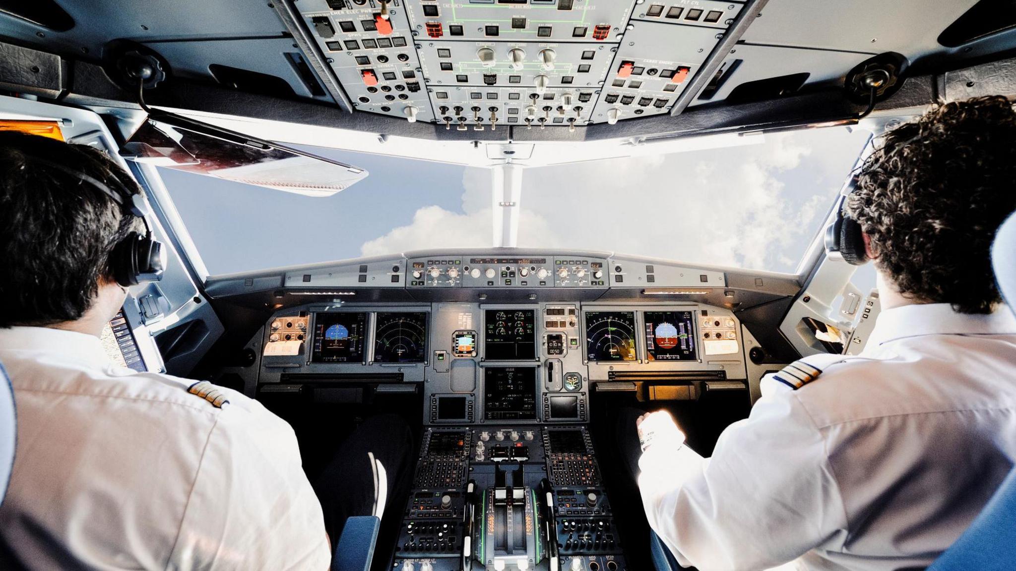 Two pilots sitting in a cockpit at plane controls.