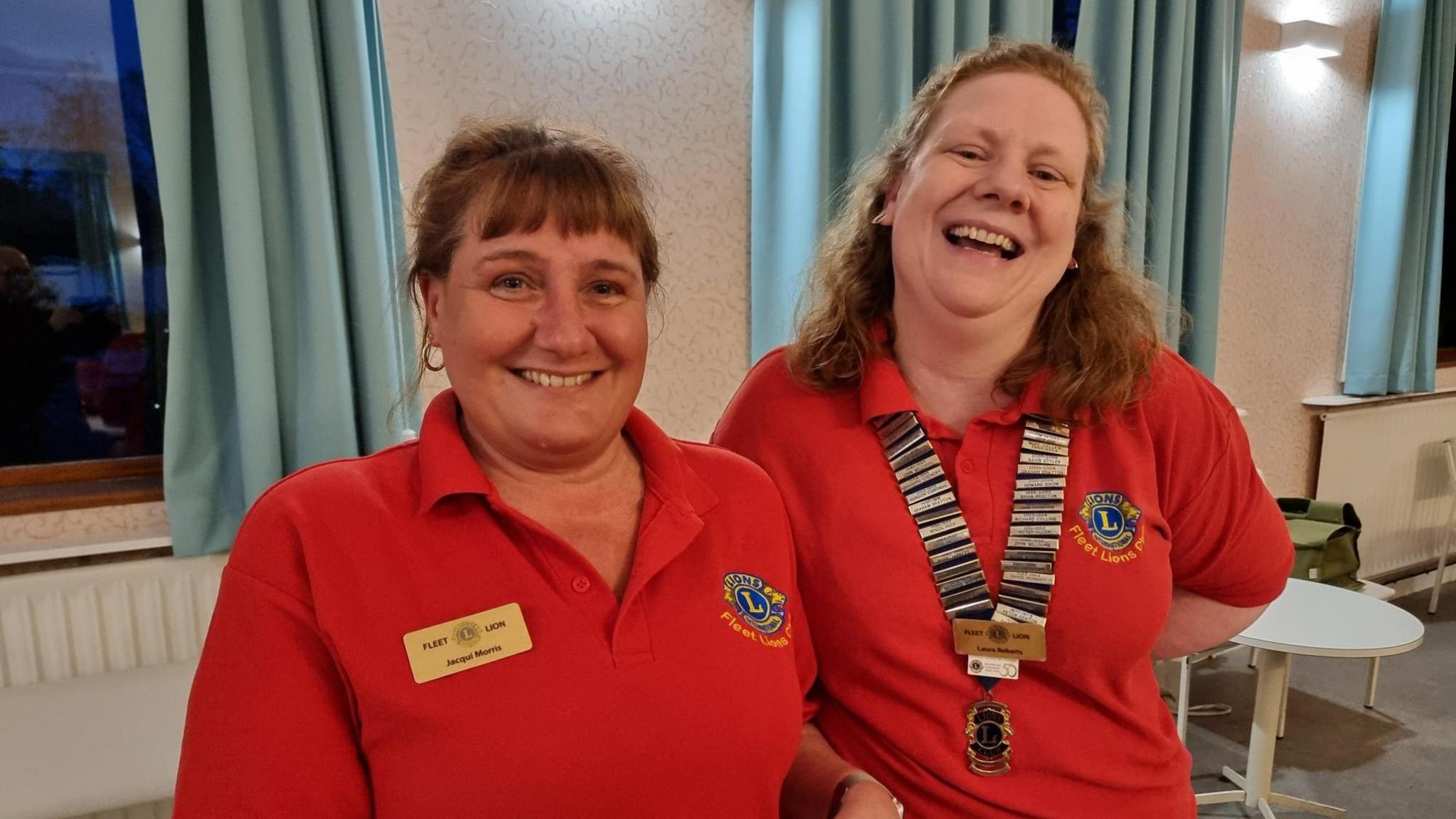 Two women smiling at the camera wearing red polo shits