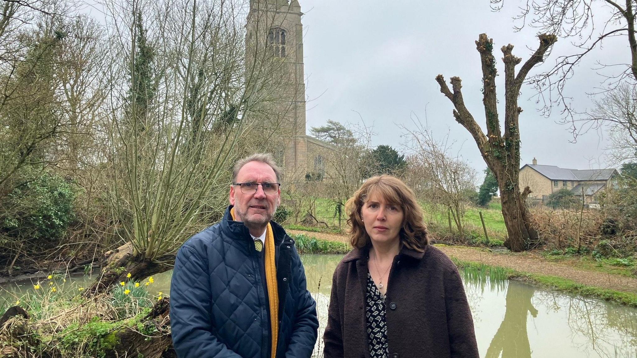 Andrew Wood and Helen Taylor looking upset in front of the pond 