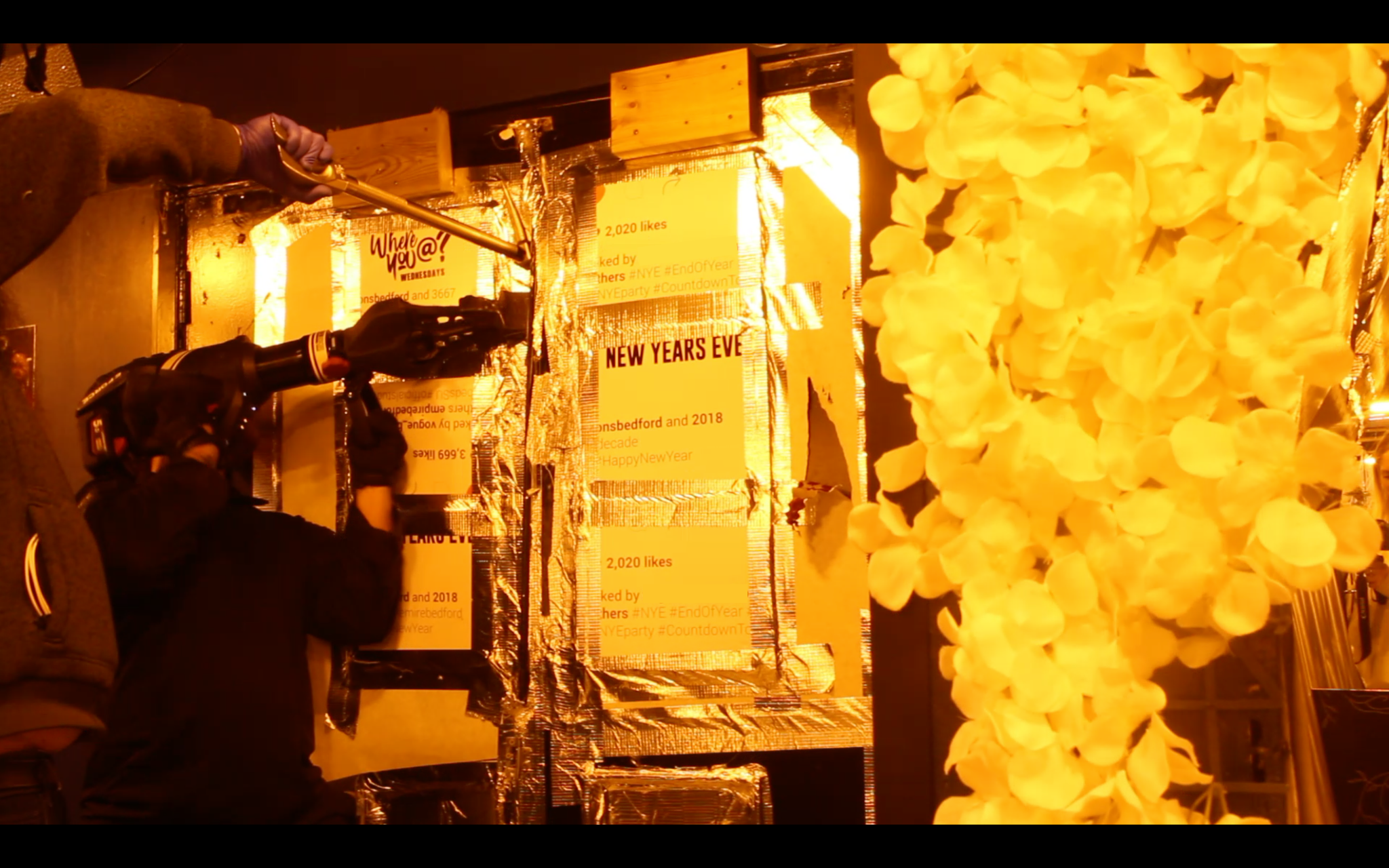 Police officers removing a wall in an nightclub. It is dark and the scene is lit by an orange light.