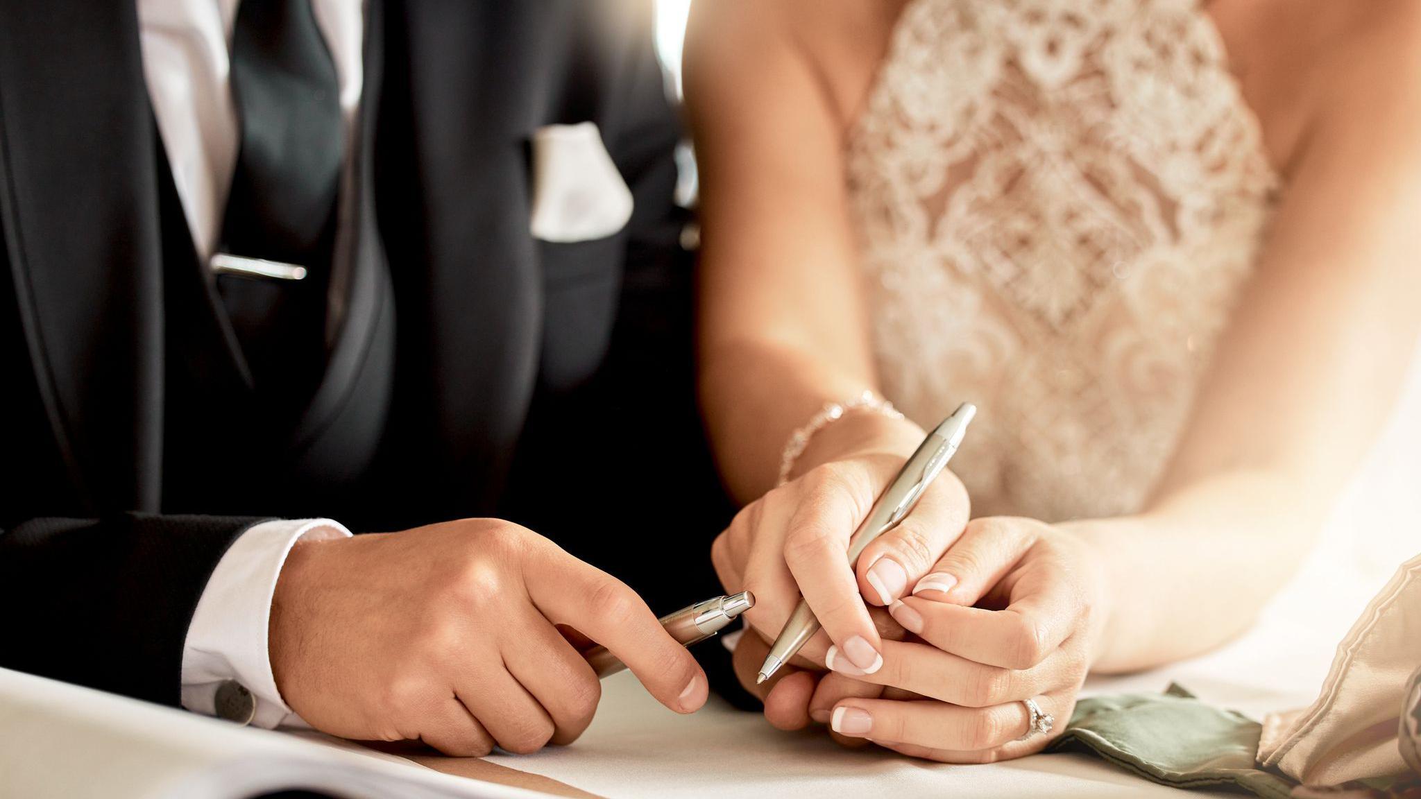 Couple sign wedding certificate, marriage registration and document paper for legal union. Closeup bride, groom and hands writing contract for celebration of love, commitment and agreement together