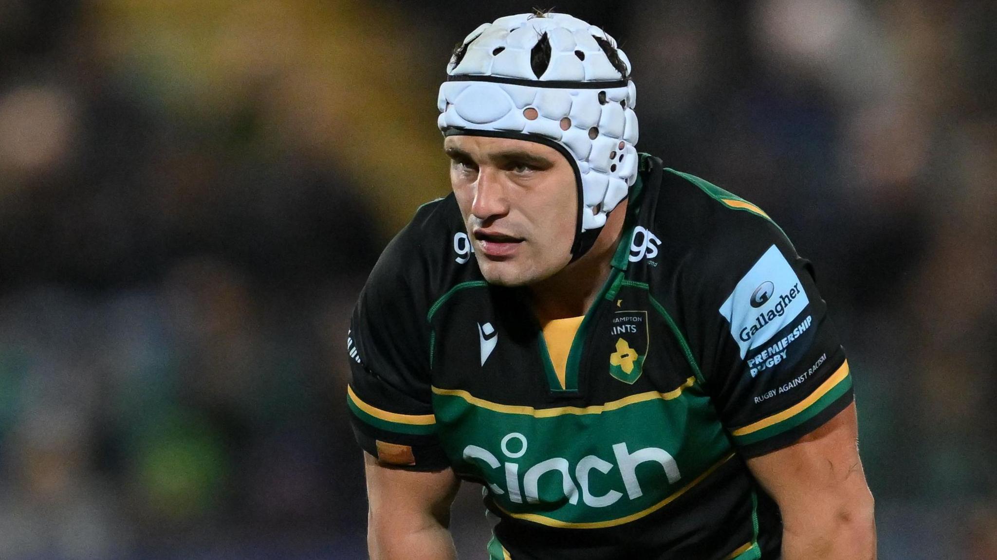 Curtis Langdon, wearing a white scrum cap, is leaning forward as if preparing to make a tackle.