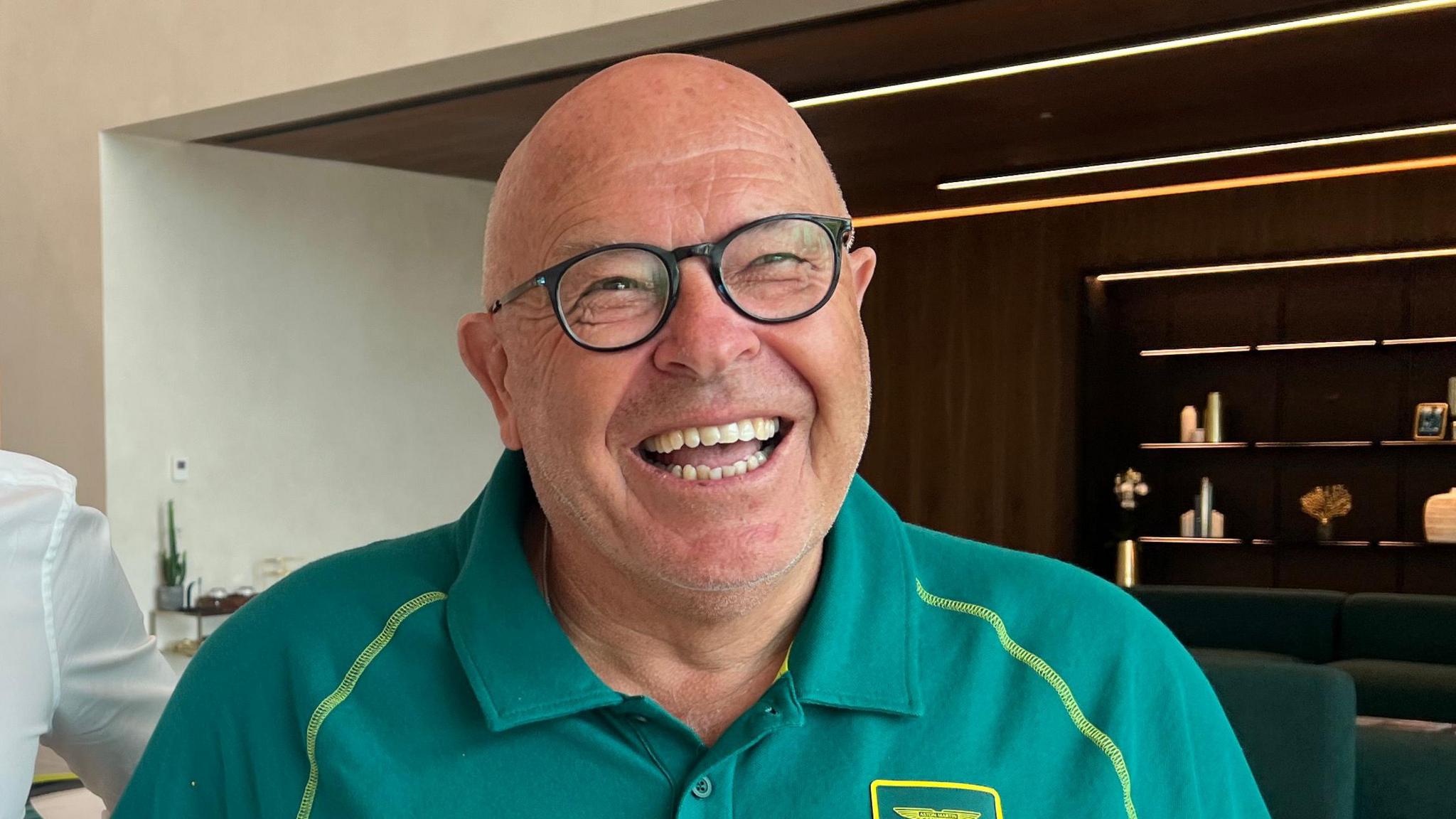 Guy Austin in a green Aston Martin F1 T-shirt. He is wearing glasses and smiling widely