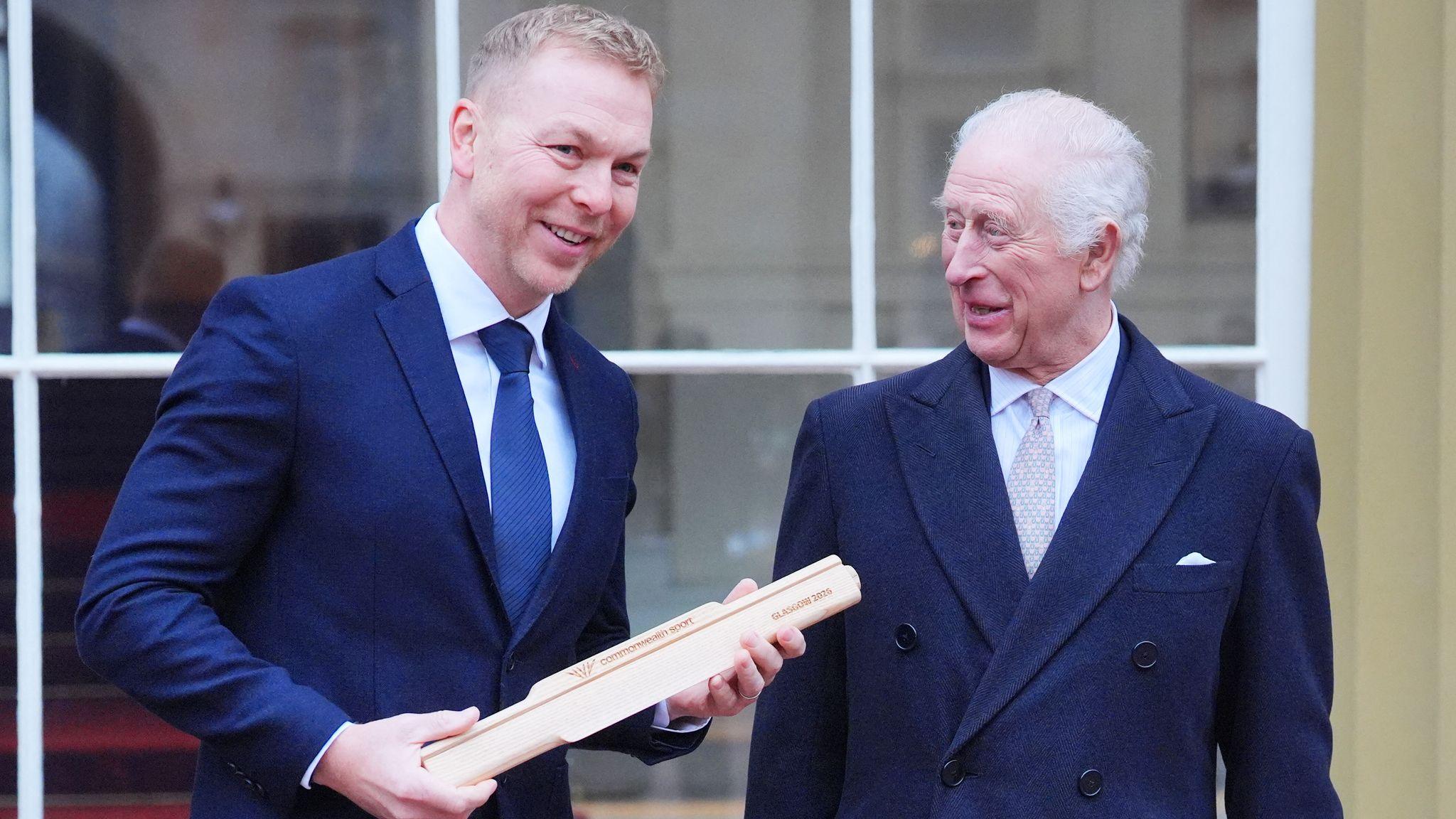 Sir Chris Hoy smiling while holding the baton next to King Charles who smiles at Hoy