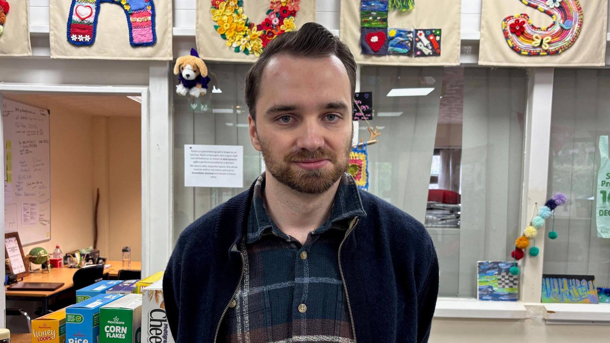 Iwan yn ei waith gyda bwydydd sydd wedi cael eu rhoid i Porthi Dre yn y cefndir.