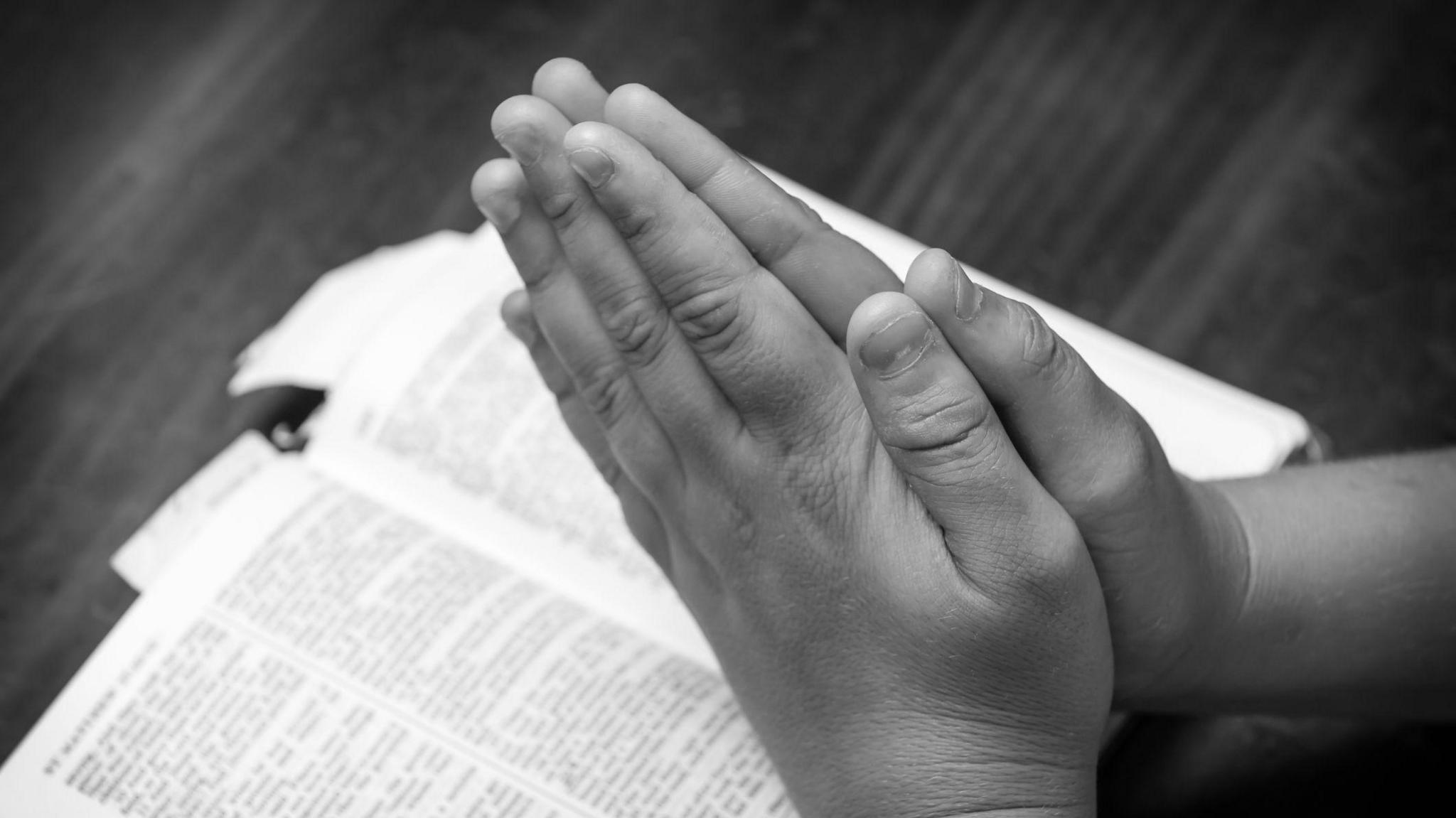 A black and white photo showing the hands of a young boy praying over the bible (stock image) 