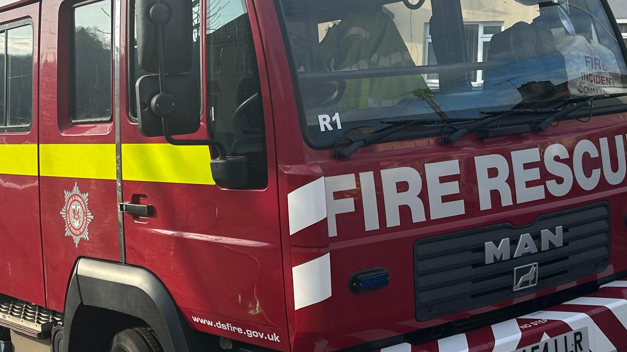 A generic shot of the front of a fire truck from Devon and Somerset Fire and Rescue Service. It is red with fire rescue across the front, a bright yellow stripe down the side and the logo