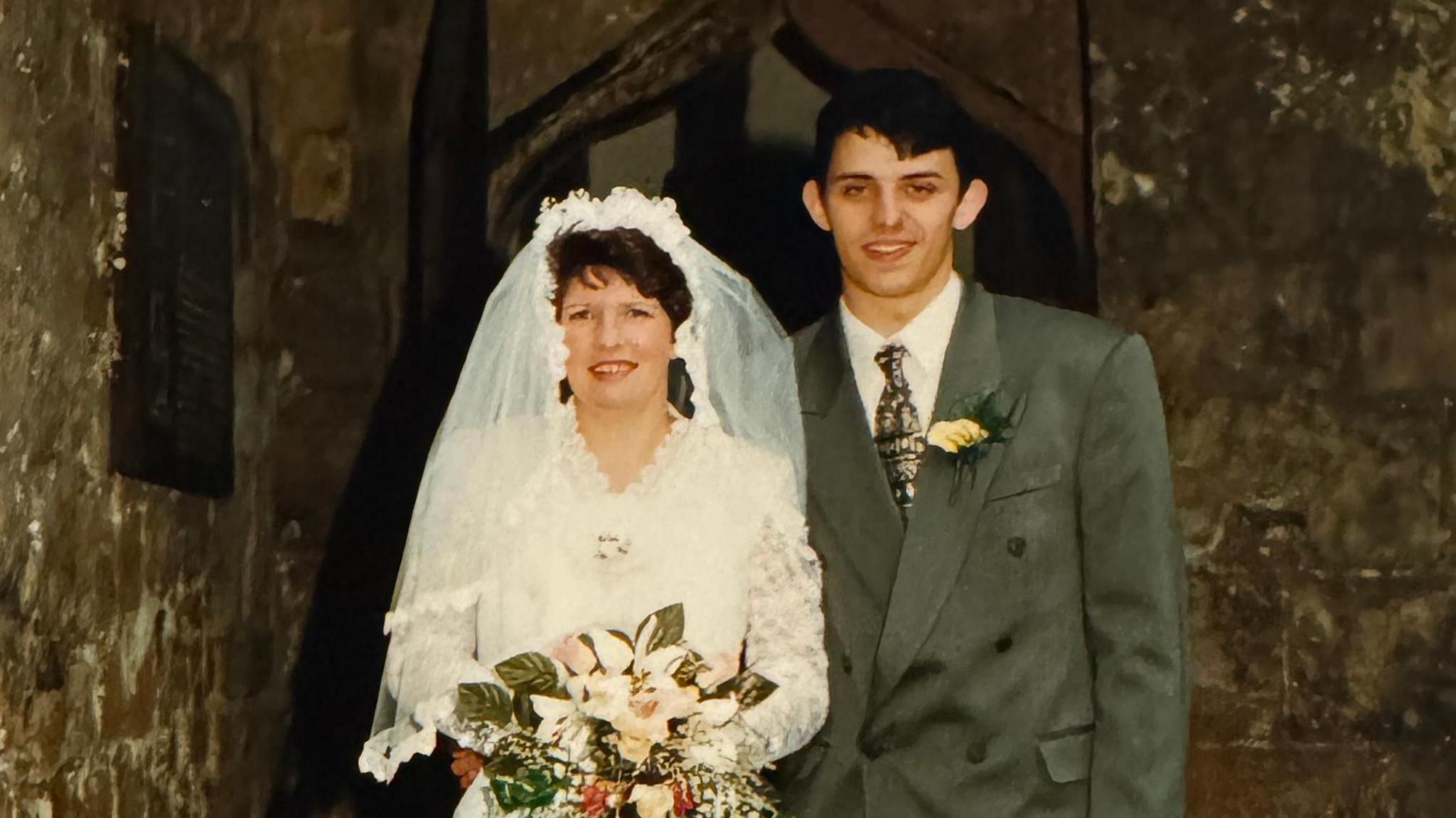 An old wedding picture of Yvonne, who is wearing a white wedding dress, and Phil, who is in a grey suit.