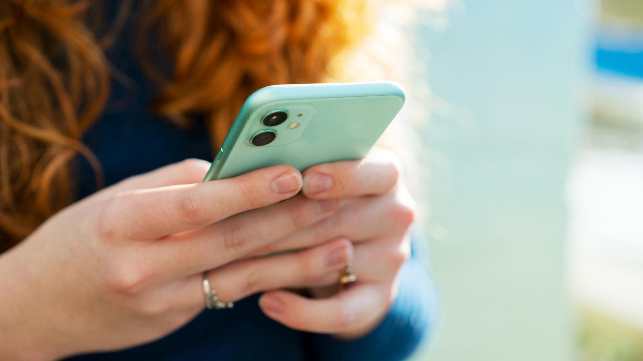 A woman with ginger hair (though you can't see her face), texting on a green mobile phone, with two rings 