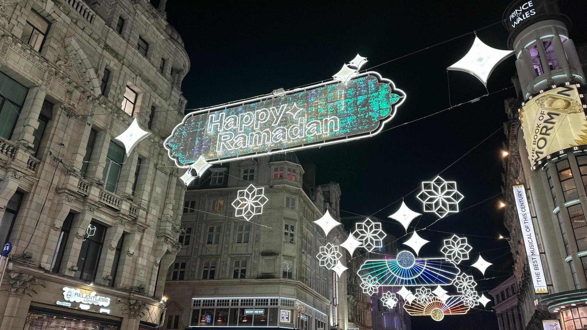 A wider picture of the words Happy Ramadan written on the light installation. It has a shiny blue green hue. 