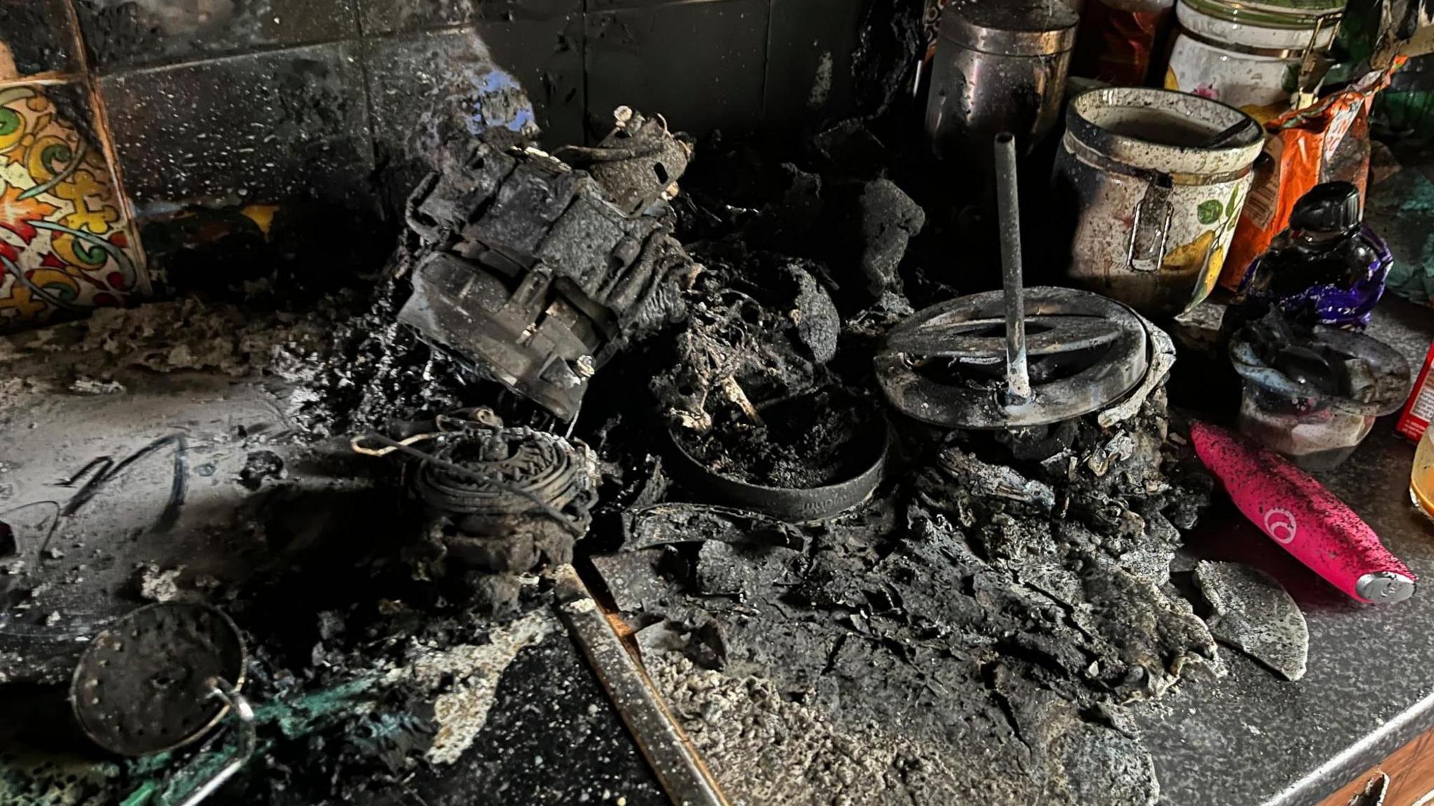 Burnt out kitchen utensils stand on a blackened kitchen work surface