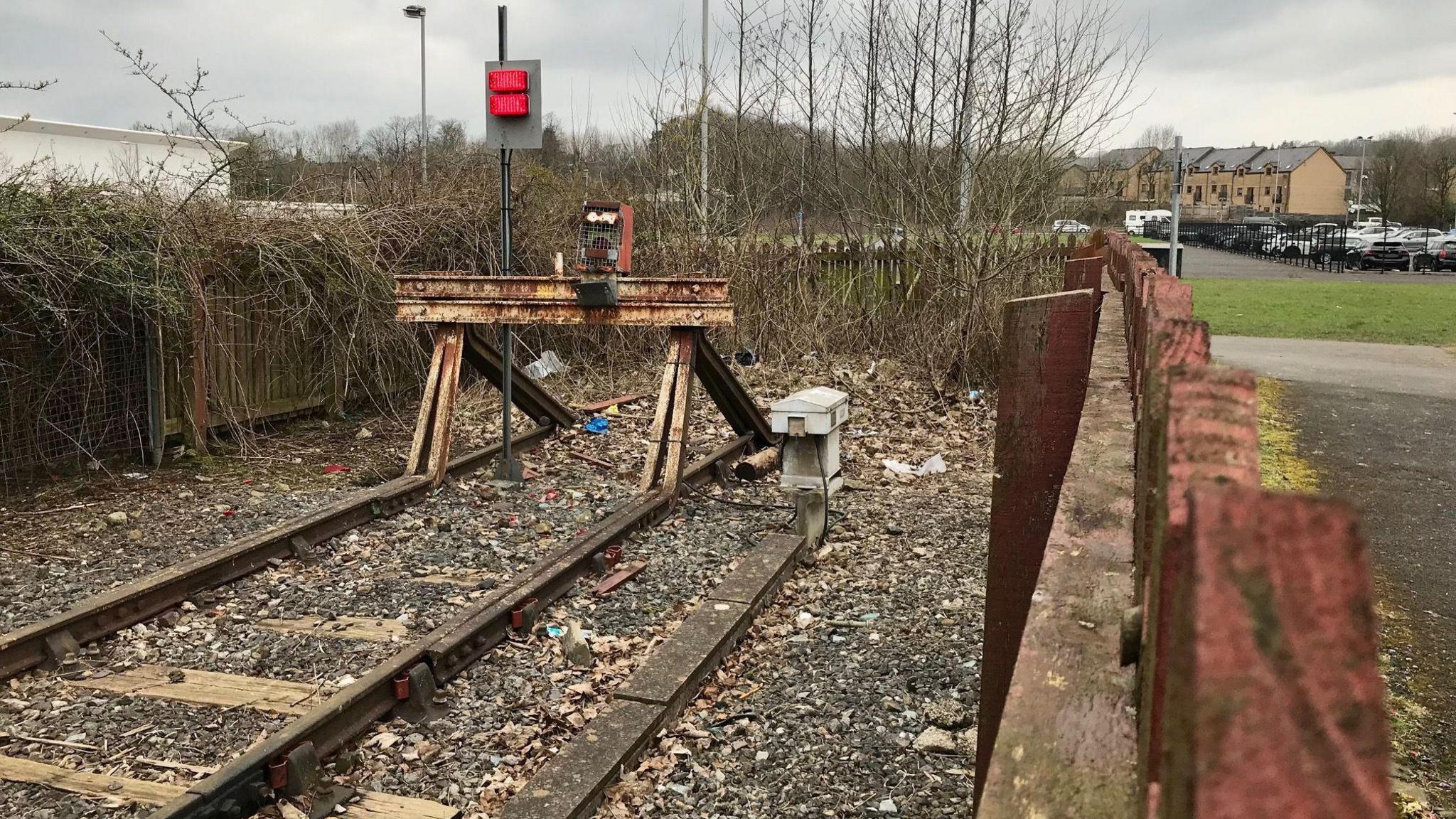 The end of the east Lancashire railway line at Colne station. The tracks run up to a wooden fence covered in barren trees. 