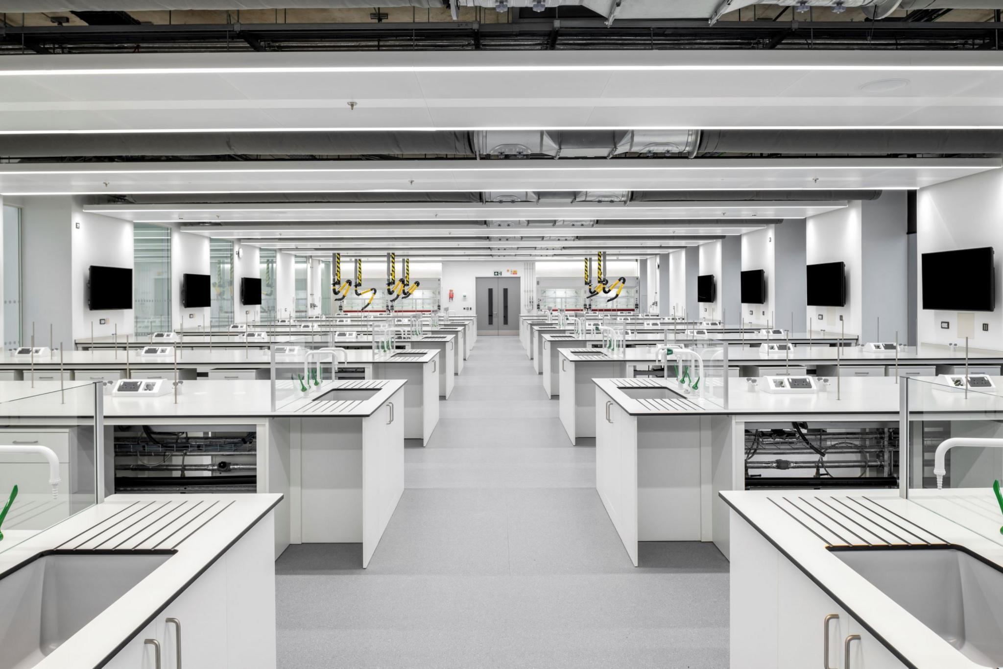 The futuristic lab space has rows of benches with sinks at the end of each row and screens at the other end