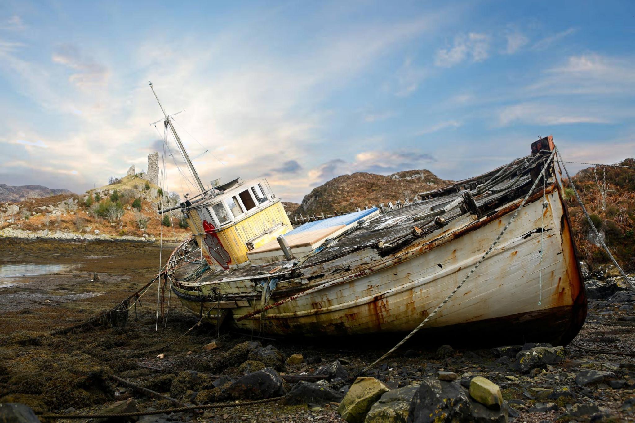 Rusty boat tilted on its side, berthed on a rocky beach