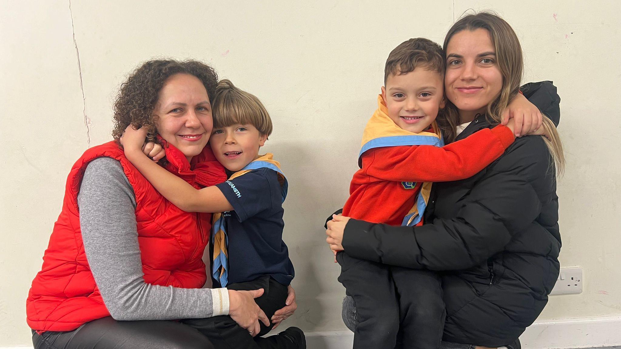 Artem and Yehor in their Squirrels uniform, hugging their mothers. All are smiling at the camera.